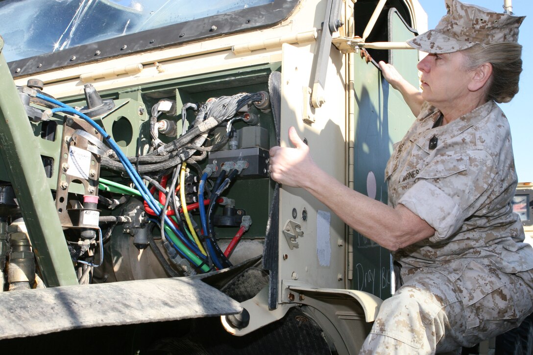 Master Gunnery Sgt. Pamela Smith climbs up to inspect the engine of a Medium Tactical Vehicle Replacement here March 17.  Smith has worked in Marine Corps motor transport for 31 years and was the first female master gunnery sergeant in the motor transport maintenance field.