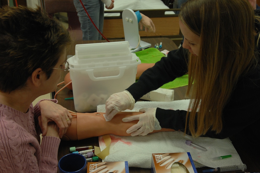 Terri Rostad, Western Dakota Technical Institute instructor, assists Stefanie Peterson, Licensed Practical Nurse program student, insert a butterfly needle into the arm of a Life Form arm simulator. Members of the LPN program will begin clinical training at the 28th Medical Group clinic on Ellsworth March 31. Students must complete 160 hours of clinical experience to obtain their degrees. (U.S. Air Force photo/Airman First Class Adam Grant)

