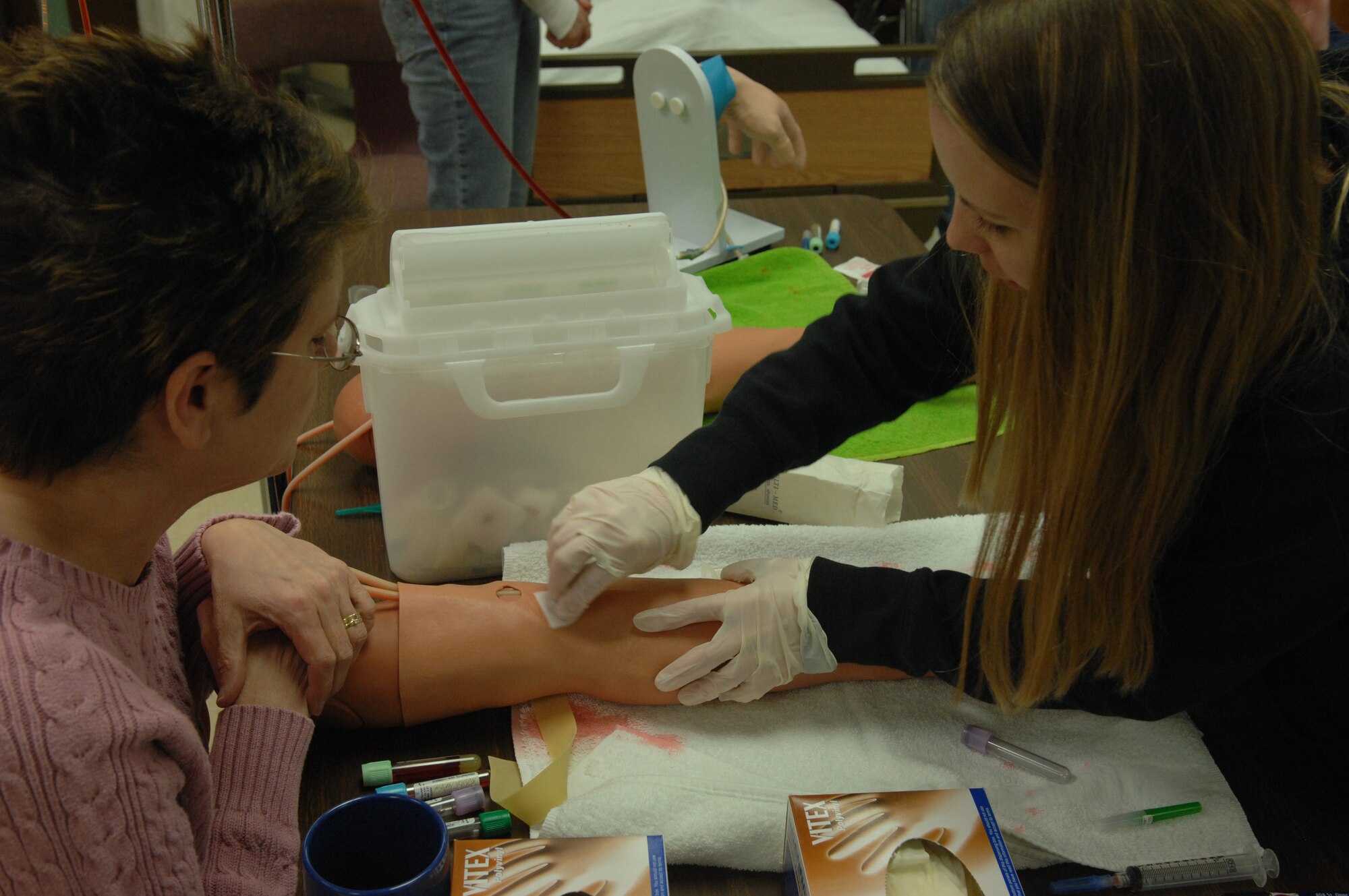 Terri Rostad, Western Dakota Technical Institute instructor, assists Stefanie Peterson, Licensed Practical Nurse program student, insert a butterfly needle into the arm of a Life Form arm simulator. Members of the LPN program will begin clinical training at the 28th Medical Group clinic on Ellsworth March 31. Students must complete 160 hours of clinical experience to obtain their degrees. (U.S. Air Force photo/Airman First Class Adam Grant)

