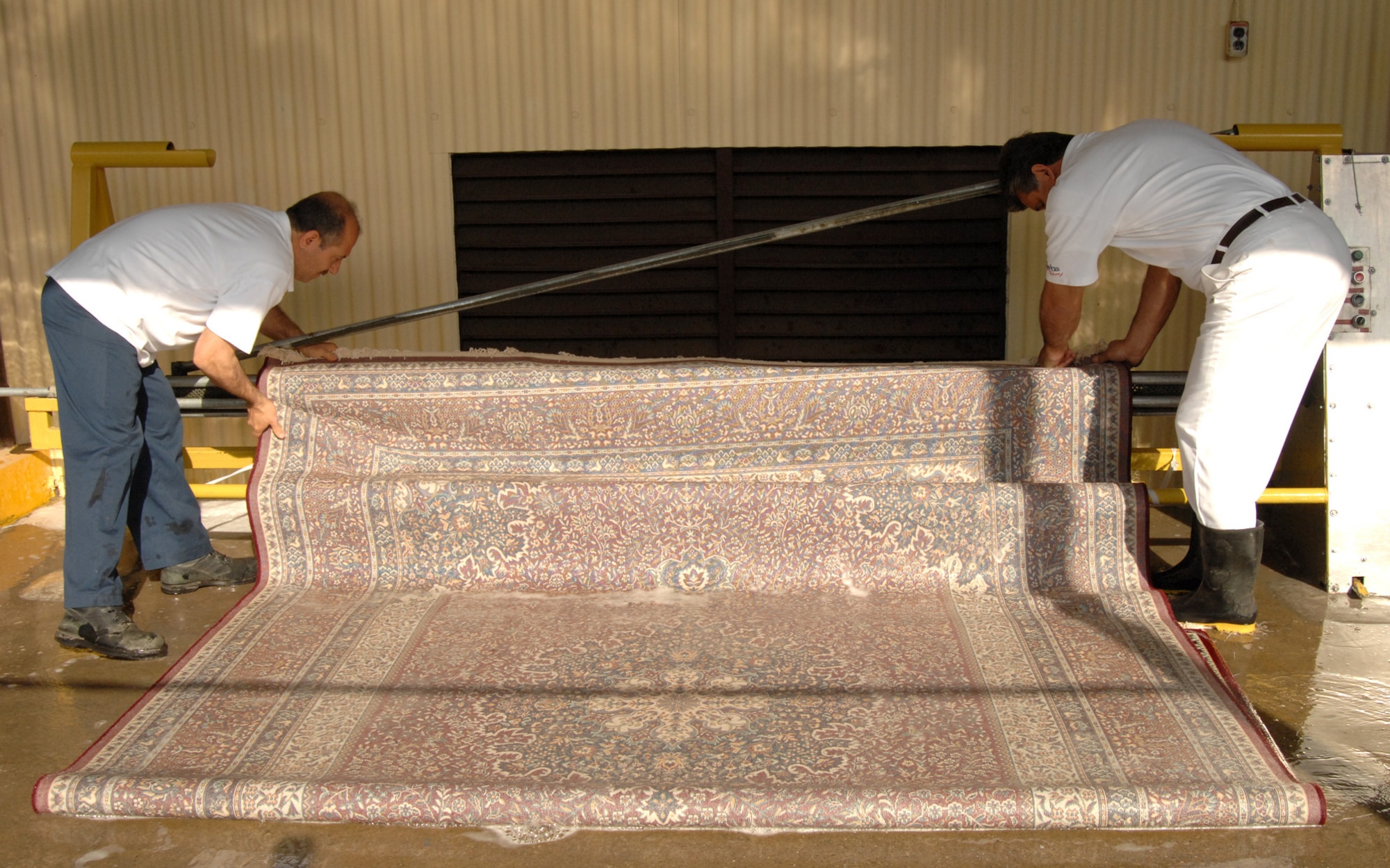 Employees at the 39th Services Squadron fabric care facility wind a carpet on to the carpet rinsing and drying machine, which was designed and built by one of their own. The new machine reduces the turn-around time of carpets from five days to just two days. (U.S. Air Force photo by Senior Airman Heather Stanton)