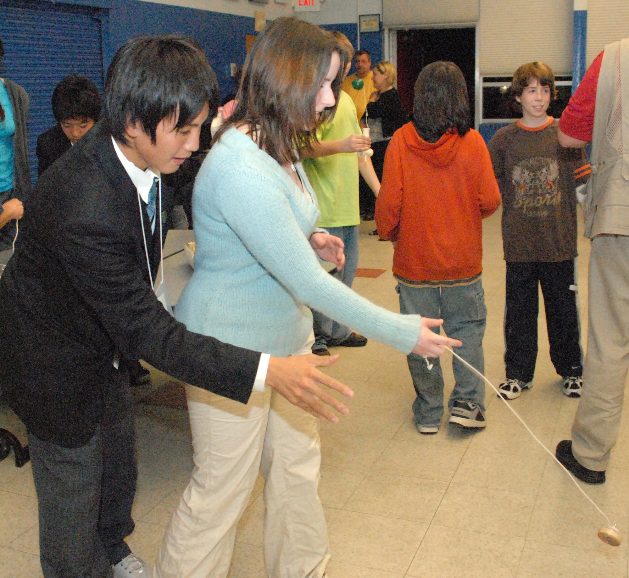 Hikaru Kuroki, a 10th-grader from  Kakuda High School in Japan, helps Teresa Anderson, a 10th-grader at Dover High School, properly throw a Japanese toy similar to both a top and a Yo-Yo March 19 here. As part of the ninth-annual Iwanuma City and city of Dover exchange program, Japanese students taught Dover students and parents about Japanese cuisine, art, and many other subjects relevant to Japanese culture. (U.S. Air Force photo/Tech. Sgt. Kevin Wallace)