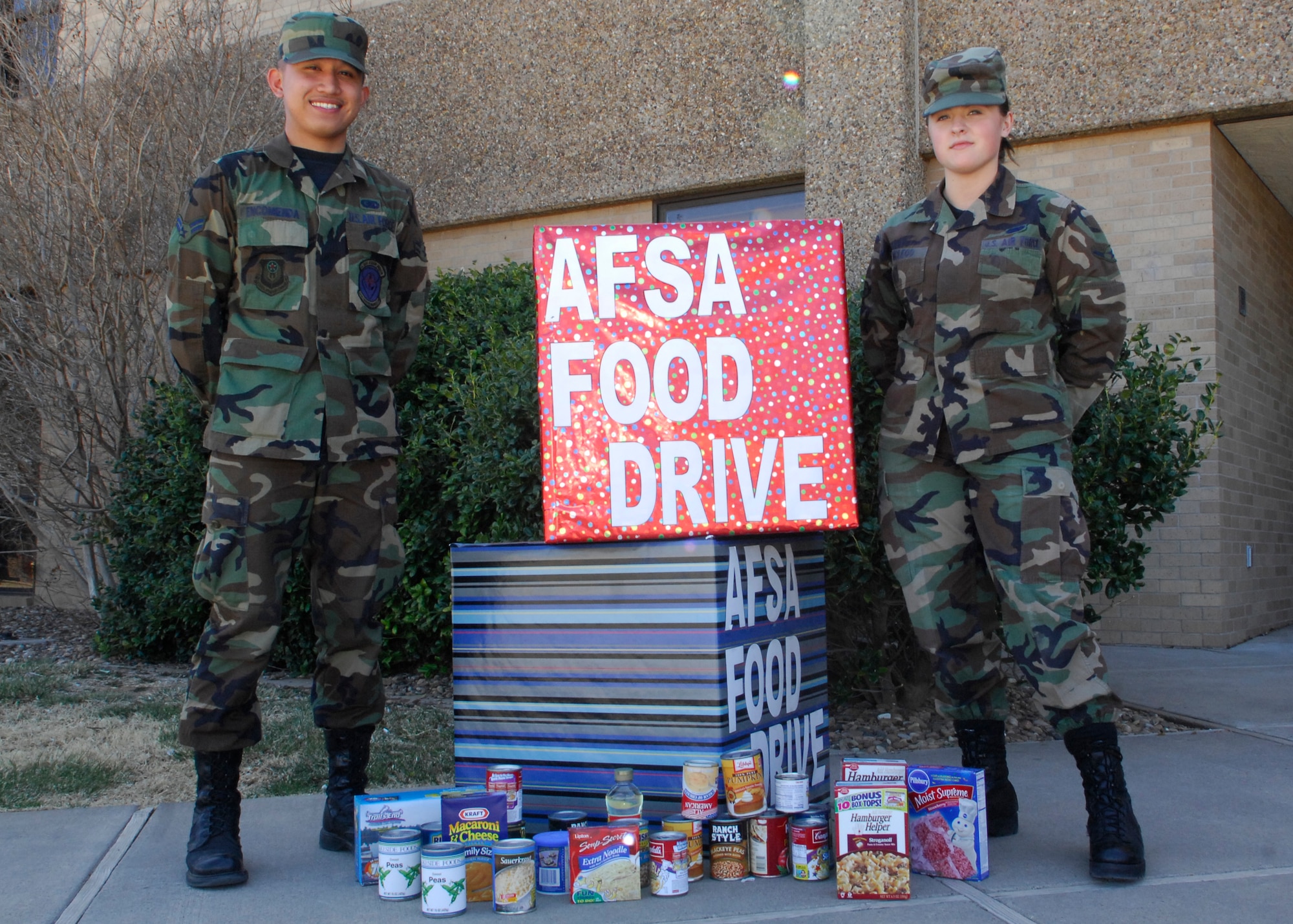 CANNON AIR FORCE BASE, N.M.- Airman 1st Class John Encomienda and Amn Natalie Mcleod, 27th Special Operations Logistics Readiness Squadron, stand in front next to two of the 12 Air Force Sergeants Association (AFSA) food drive boxes they built. The Airmen originally built and placed six boxes at various locations on base, but had to build another six because of the success of the drive. AFSA provided the money for the box decorations. (U.S. Air Force photo by Airman 1st Class Erik Cardenas)