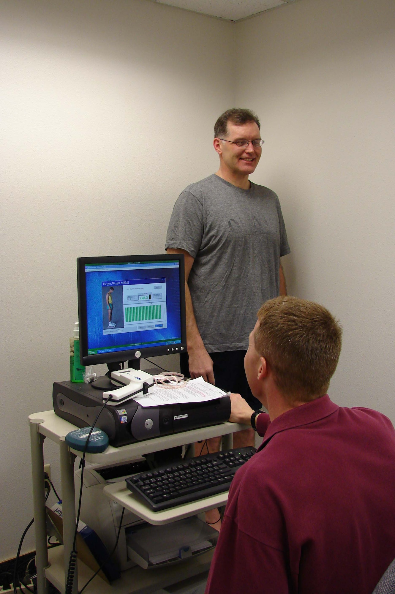 Jerry Kain, stanidng on the scale, and Kirk Clark share a laugh during the third assessment visit for the Largest Loser program March 11. Mr. Kain learned he had lost 26.8 pounds, three-and-a-half inches from his waist and a total of three percent body fat up to that point. (U.S. Air Force photo/Valerie Mullett)