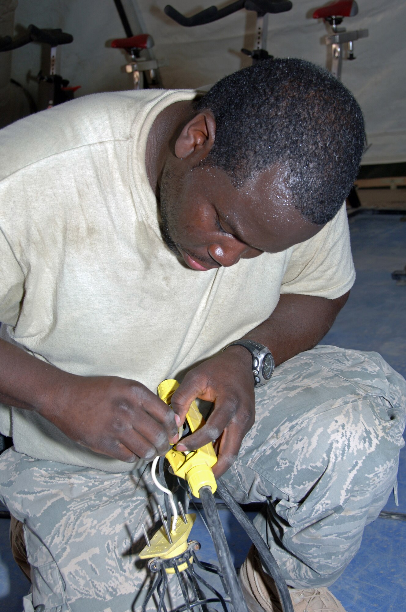 ALI BASE, Iraq -- Senior Airman Kevin Dowdye, 407th Air Expeditionary Group member, repairs a light fixture before hanging it up in the temporary fitness facility March 21.  Airman Dowdye is an electrical systems journeyman deployed from Eielson AFB, Alaska.  (U. S. Air Force photo / Tech. Sgt. Sabrina Johnson)