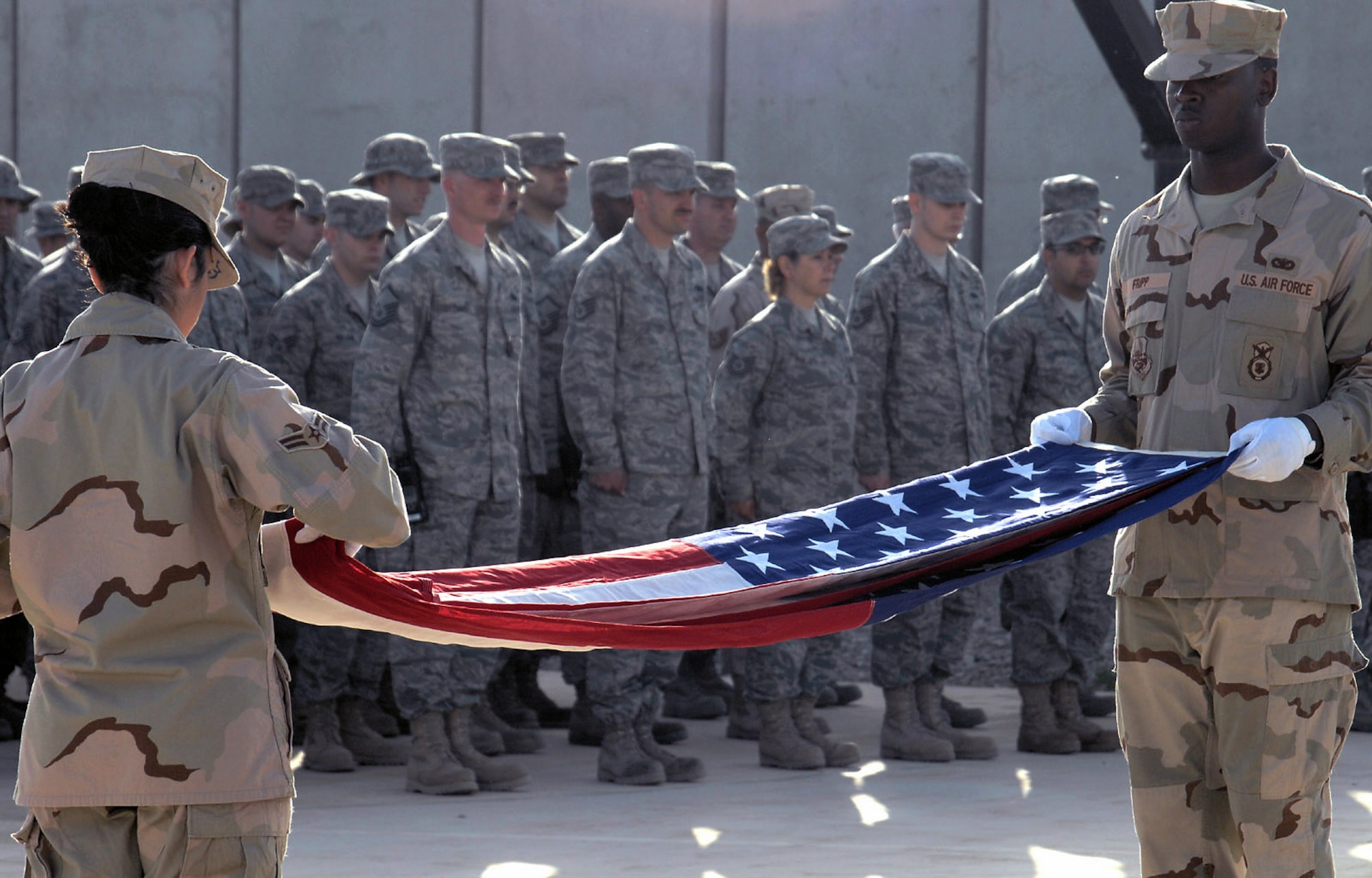 Airman 1st Class Frances Anderson and Senior Airman Terryl Fripp perform a flag-folding ceremony during an Operation Iraqi Freedom Anniversary Commemoration March 20 at Kirkuk Air Base, Iraq. The ceremony focused on the sacrifices of the 42 Airmen who gave their lives supporting the war in Iraq. (U.S. Air Force photo/Senior Airman SerMae Lampkin) 
