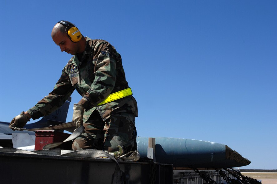 DYESS AIR FORCE BASE, Texas -- Airman 1st Class Adam Aleweidat, 7th MUNS, runs a strap through a container in preparation to secure it, March 19. Bombs and tools used to load and unload a B-1 bomber are transported using a flat-bed trailer truck. (U.S. Air Force photo by Senior Airman Courtney Richardson)