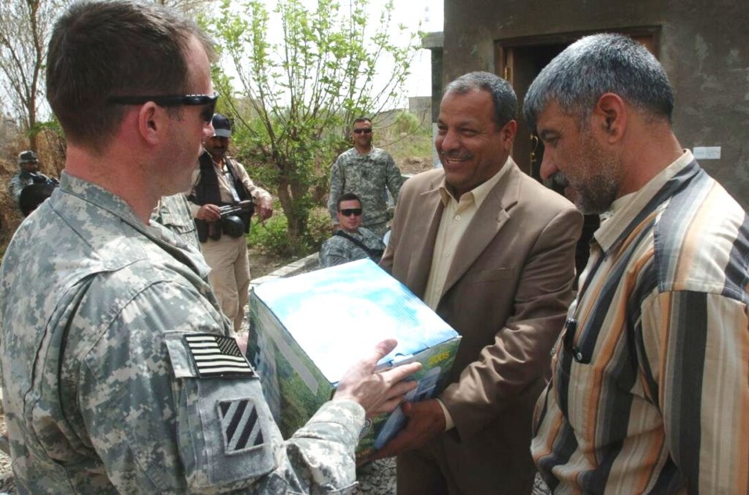 Army Lt. Col. John Kolasheski, commander of 3rd Squadron, 1st Cavalry Regiment, gives Mahmud Jabllawe, the leader of the Sons of Iraq group in Tuwaitha, a small village east of Baghdad, a house-warming gift before their meeting at Jabllawe’s house, March 21, 2008. Photo by Spc. Ben Hutto, USA