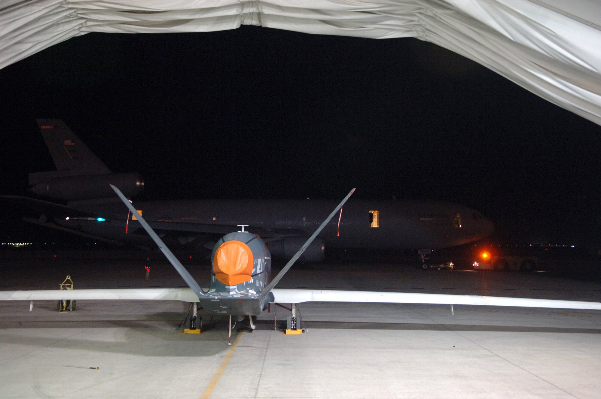 A KC-10 Extendor is towed to a parking spot while a Global Hawk unmanned aerial vehicle waits to be prepared for take off from a Southwest Asia air base. (U.S. Air Force photo/Senior Airman Levi Riendeau)
