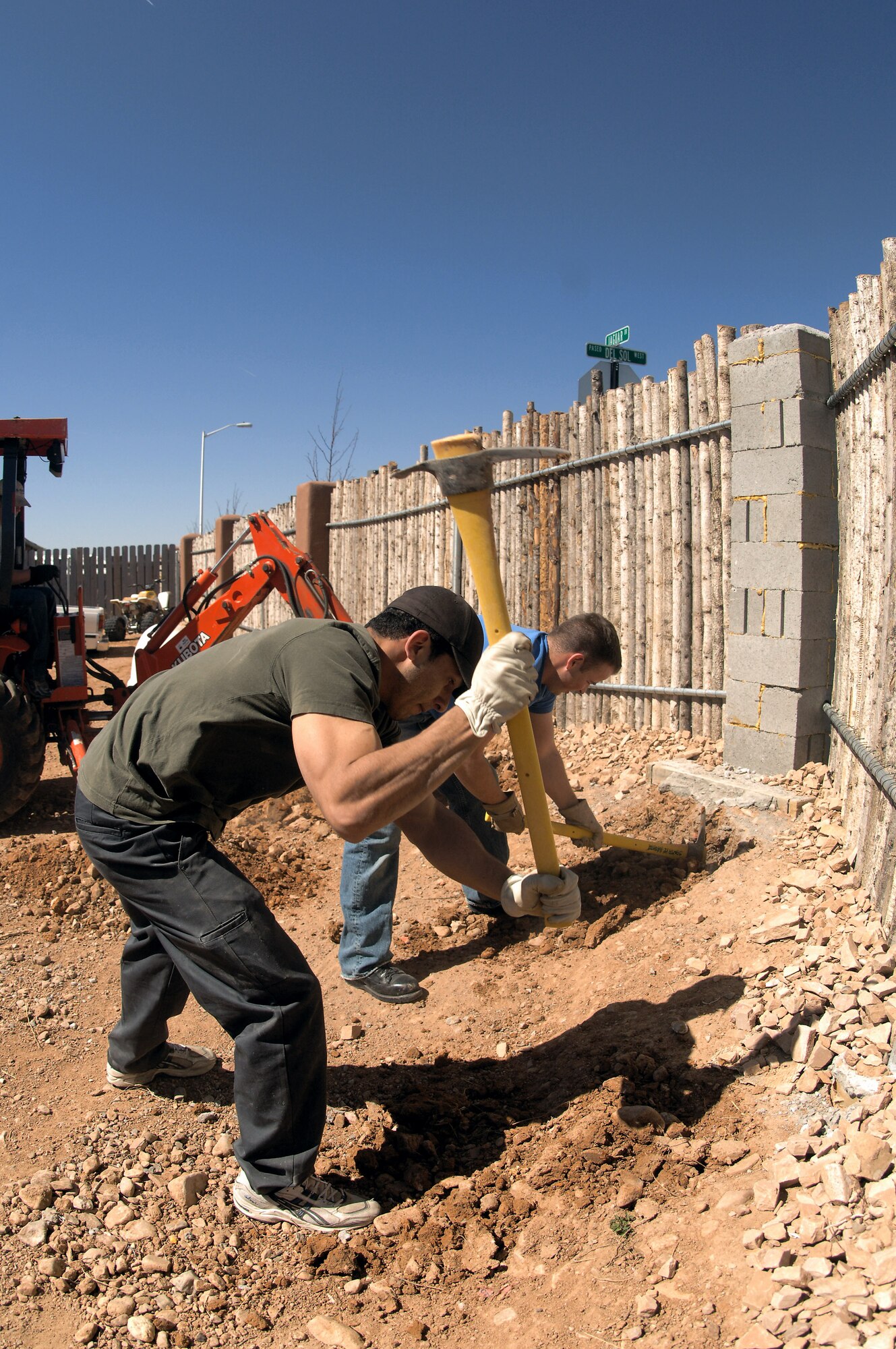 Cadet 2nd Class Francisco De La Torre, front, and Cadet 2nd Class Grant Smith use pick-axes to start leveling the landscape of the yard at a completed Habitat for Humanity home. Cadets De La Torre and Smith are two of 65 Air Force Academy cadets giving up their spring break this week, to build homes for the needy in Santa Fe, N.M.; Cody, Wyoming; El Paso, Texas; and Beaumont, Texas. (U.S. Air Force photo/John Van Winkle)