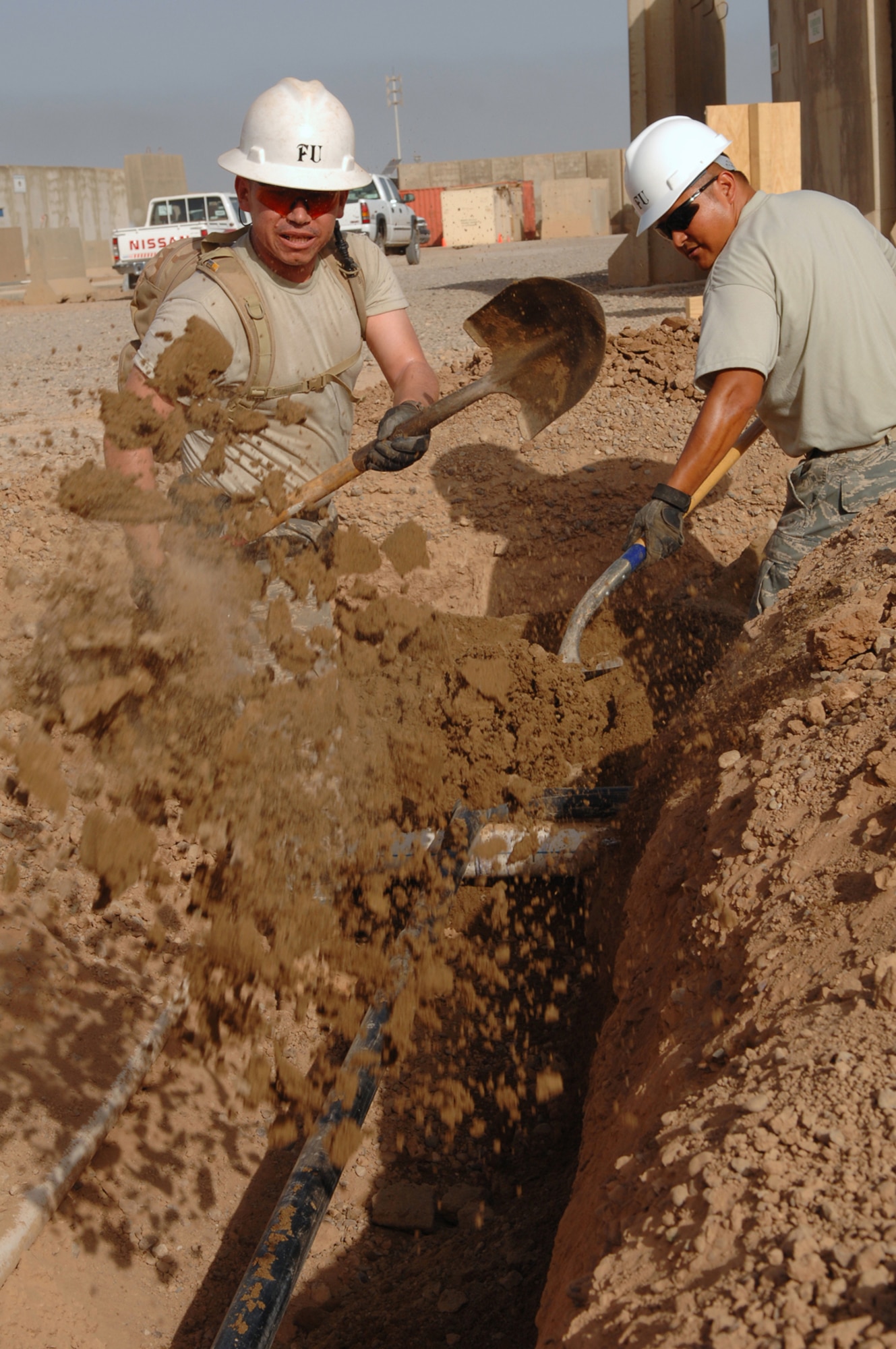 BALAD AIR BASE, Iraq -- Senior Airmen Antonio Martinez and Juan Reynoso, 332nd Civil Engineer Squadron plumbers, shovel soft sand over new piping here, March 24. The sand will protect and cushion the newly installed pipes in the Air Force housing area from rocks. The pipe infrastructure replacement project is scheduled to be completed by mid-June. Both Airmen are deployed from Peterson Air Force Base, Colo. (U.S. Air Force photo/ Senior Airman Julianne Showalter)