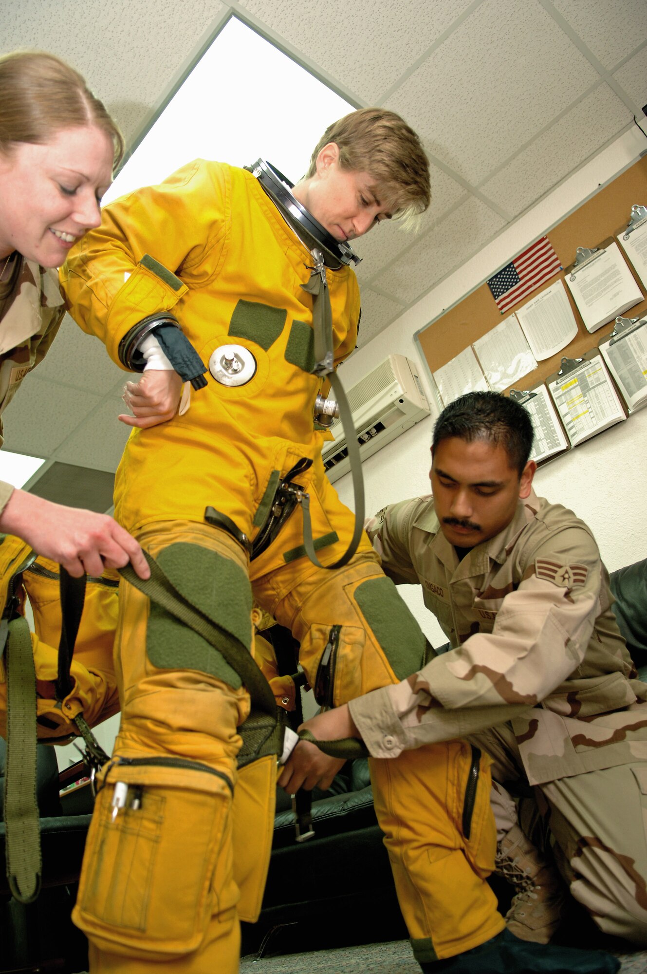 Capt. Heather Fox, a U-2 Dragon Lady pilot with the 99th Expeditionary Reconnaissance Squadron, stands while Senior Airman Roric Ongaco (right) and Staff Sgt. Lisa Tetrick, 99th ERS physiological support division technicians, help attach the torso harness to her suit.  She was preparing to fly a reconnaissance mission March 25 from an air base in Southwest Asia.  Captain Fox is one of only three female U-2 pilots currently serving in the Air Force.  (U.S. Air Force photo/Senior Airman Levi Riendeau) 