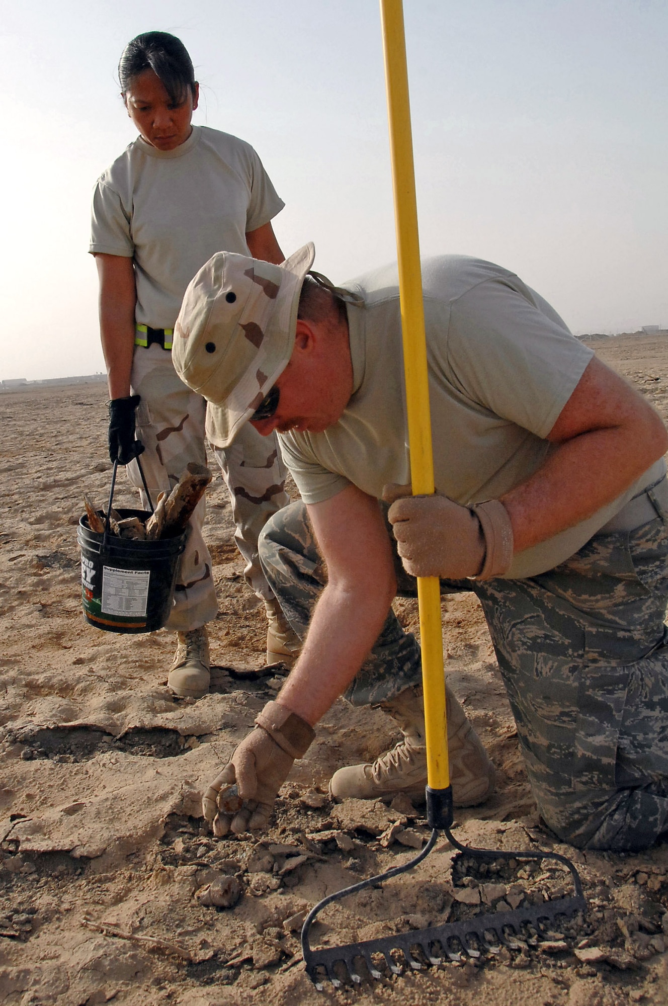 Master Sgt. Curtis Keel uncovers ordnance debris as Tech. Sgt. Maria Adams observes March 26 at Ali Base, Iraq. Explosive ordnance disposal team members and augmentees scoured 159 acres of unexploded ordnance fields picking up debris and marking un-removable items for detonation. The Airmen are members of the 407th Air Expeditionary Group. Sergeant Keel is a EOD member deployed from Kirtland Air Force Base, N.M. and Sergeant Adams is a supply craftsman deployed from Spangdahlem AB, Germany. (U.S. Air Force photo/Tech. Sgt. Sabrina Johnson) 