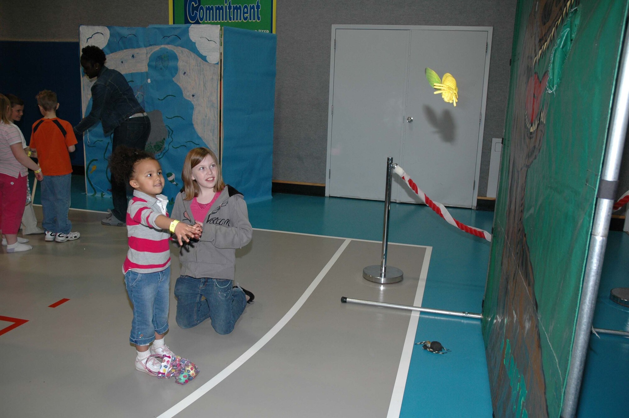 Little Warrior Kayla, 4, tosses a stuffed insect into the mouth of a dinosaur while Sierra, 11, looks on at the Jurassic Toss during the Youth Programs Spring Carnival, March 22. (U.S. Air Force photo/Airman 1st Class Emerald Ralston)