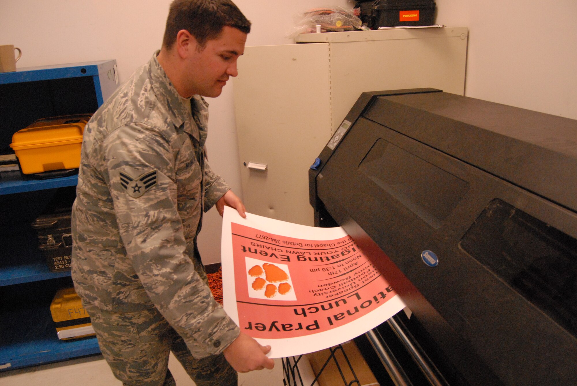Senior Airman Travis McMillion, 43rd Maintenance Squadron, removes the sticker for the 43rd Airlift Wing Chapel's National Prayer Luncheon event from the squadron's printer/plodder/cutter machine. 43rd MXS uses the machine to make squadron patch stickers, labels and other posters for the base. (U.S. Air Force Photo by 2nd Lt. Chris Hoyler)