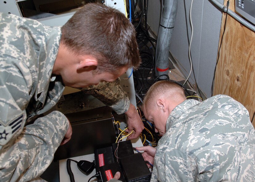DYESS AIR FORCE BASE, Texas -- Staff Sergeant Nicholas Siburt and Senior Airman Brandon Allen reattach wires coming from the back of a digital signal transmitter in the base command post. The digital signal transmitter relays radio transmissions to handheld and corded radios. (U.S. Air Force Photo by Airman 1st Class Micheal Breaux)