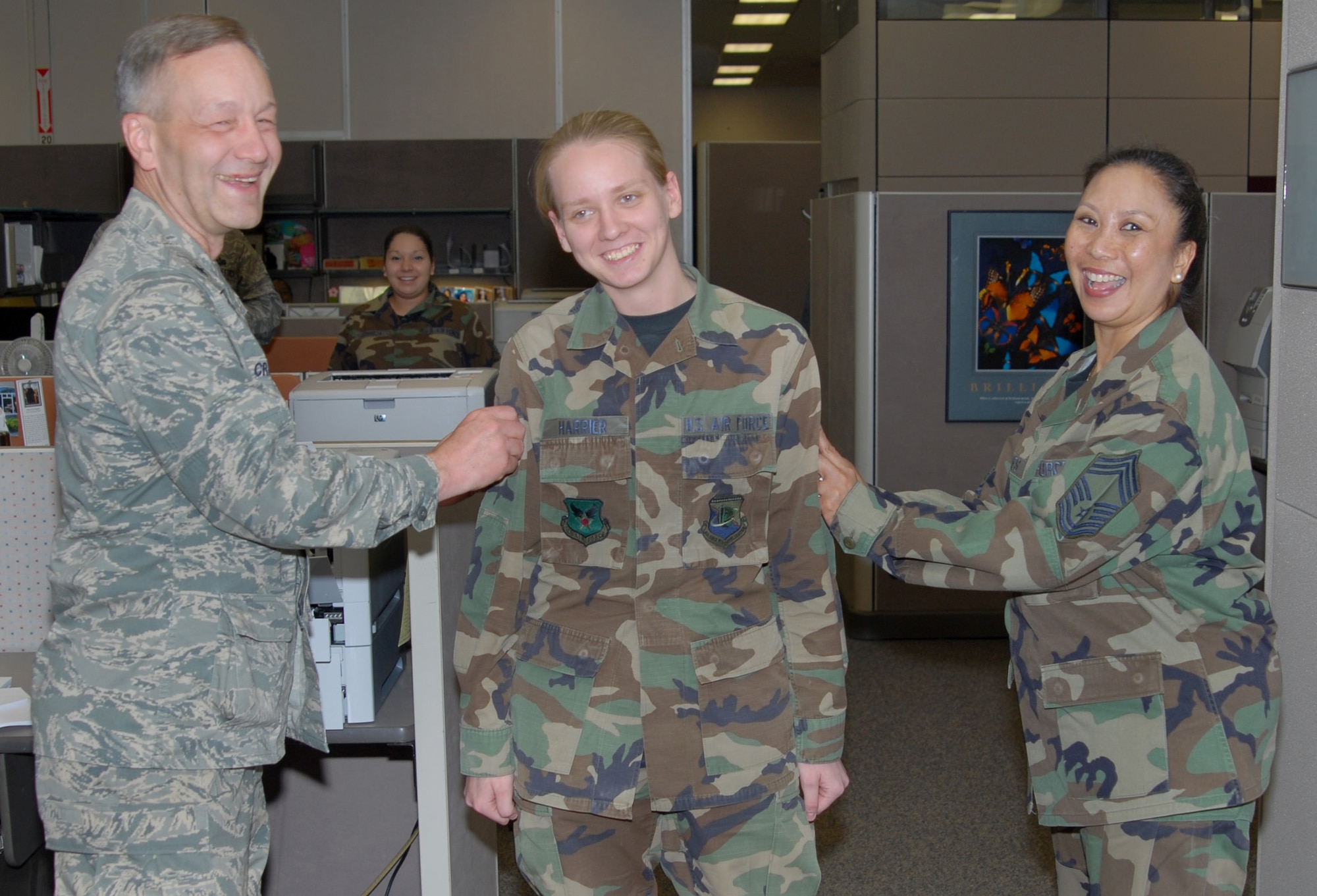 Airman Lacey Harrier, DPS, is tacked by Brig. Gen. Eric Crabtree (left), ARPC commander, and Chief Master Sgt. Fatima Jones, DPS, in the contact center March 27. Airman Harrier is one of several ARPC Airmen who will be promoted at an official ceremony March 31. (U.S. Air Force photo/Ellen Edwards)