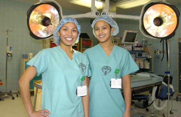 Airmen Taija Alcantara (left) and Tiamae Cruz pose together in an operating room where they are in training to become surgical technicians. Their military careers have continued to follow each other since they joined under the Air Force Buddy System in Guam. Photo by Chuck Roberts