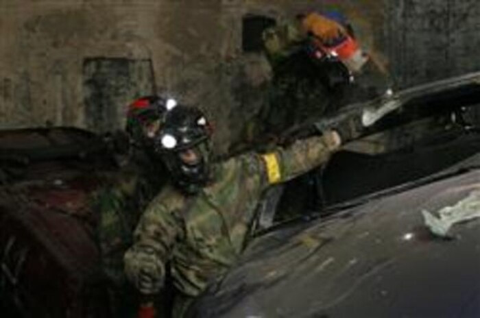 Petty Officer 3rd Class Matthew Esper (top), a hospital corpsman assigned to Headquarters and Service Company, Chemical Biological Incident Response Force, II Marine Expeditionary Force, reaches a casualty trapped inside a car by cutting the windshield. Lance Cpl. Joshua Foster (right) and Cpl. Thomas Downes (left), both technical rescue technicians, Technical Rescue Platoon, Headquarters and Service Company, assist in the evacuation. The simulated chemical attack included several mock car wrecks alongside the highway here March 25-30.