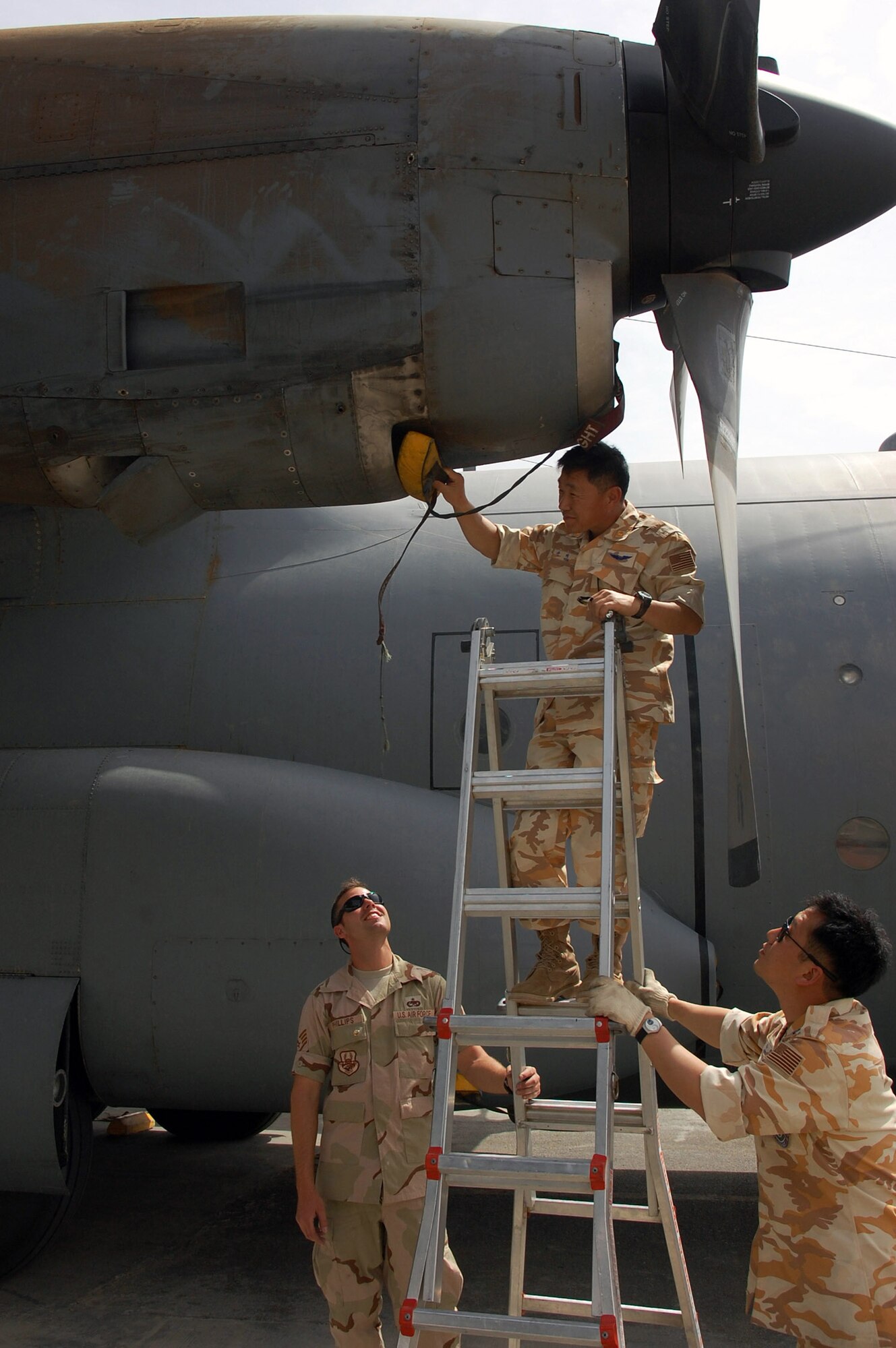 South Korean Warrant Officer Hae Ok Yoon (center) inserts an oil cooler intake plug into a C-130 Hercules while Staff Sgt. William Phillips (left) and South Korean Master Sgt. Jun Wan Park keep the ladder steady for him March 26 at a Southwest Asian air base. Airmen from the U.S., Japanese Air Self-Defense Force and South Korean air force's 58th Airlift Wing participated in a coalition maintenance exchange program allowing maintainers to sharpen their skills, exchange ideas, and promote closer relations among coalition air forces supporting the war on terrorism. Warrant Officer Yoon and Sergeant Park are from the South Korean air force's 58th Airlift Wing, and Sergeant Phillips is a crew chief deployed to the 386th Expeditionary Aircraft Maintenance Squadron. (U.S. Air Force photo/Staff Sgt. Patrick Dixon) 
