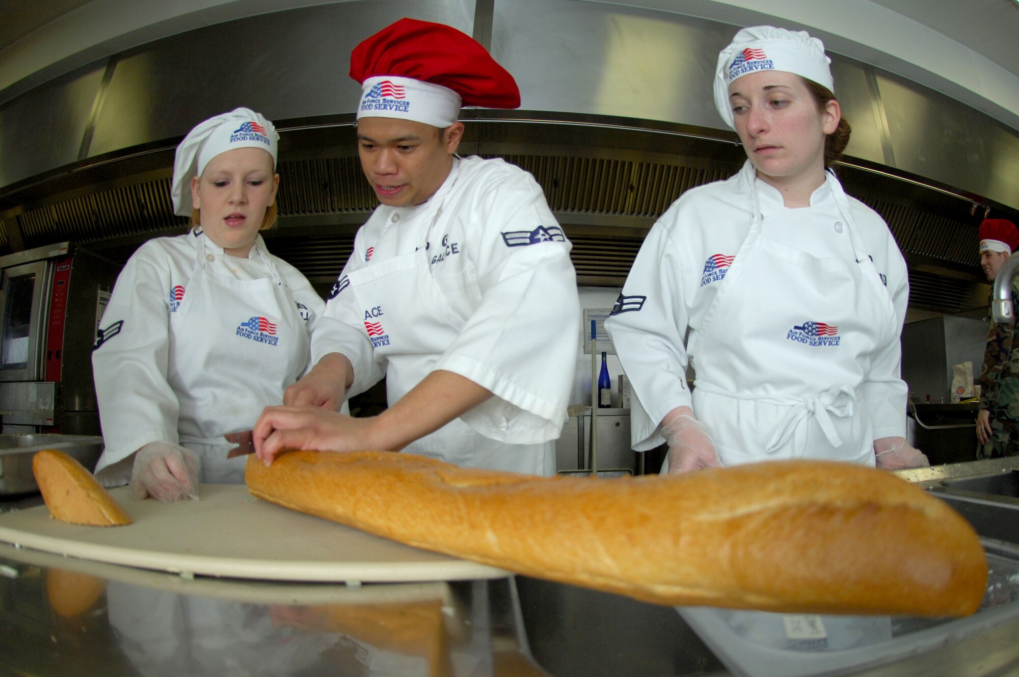 435th Services Squadron members, airmen first class Amber Hill (left) and Katherine Thompson, watch team leader, Billy Joe Galace, slice frozen bread during Ramstein's Iron Chef competition March 27. The competition is set to be held quarterly to help build camaraderie amongst Airmen. Photo by Senior Airman Melissa Sheffield