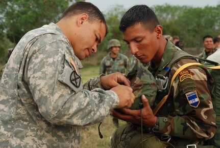 Capt. Charles Faison, 509th Airborne Battalion, Ft. Polk, La., helps a Honduran "paracaidista" repair his helmet before the combined jump with U.S. and Honduran soldiers April 30. The 509th was in Honduras to exchange ideas with Honduran military members in preparation for a multi-national exercise in August. (U.S. Air Force photo by Tech. Sgt. John Asselin)
