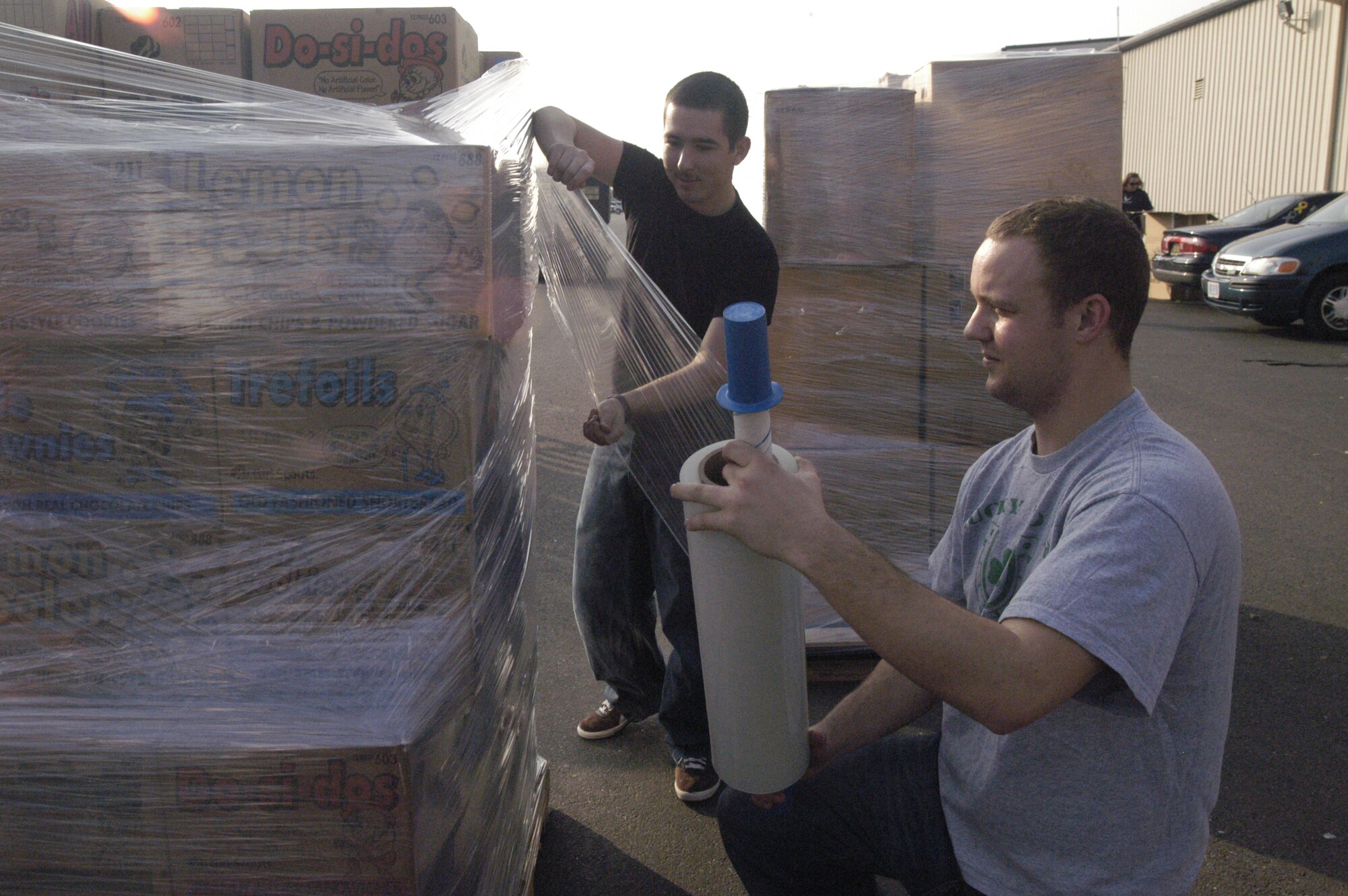 (Left to right) Airman 1st Class Robert Klein, 436th Maintenance Squadron crew chief, and Airman 1st Class Michael McKee, 436th Aircraft Maintenance Squadron crew chief, wrap one of several pallets of Girl Scout cookies to help USO Delaware sort and organize donated times. Airmen palletized more than 5,000 boxes of Girl Scout cookies. (U.S. Air Force photo/Airman 1st Class Shen-Chia Chu)