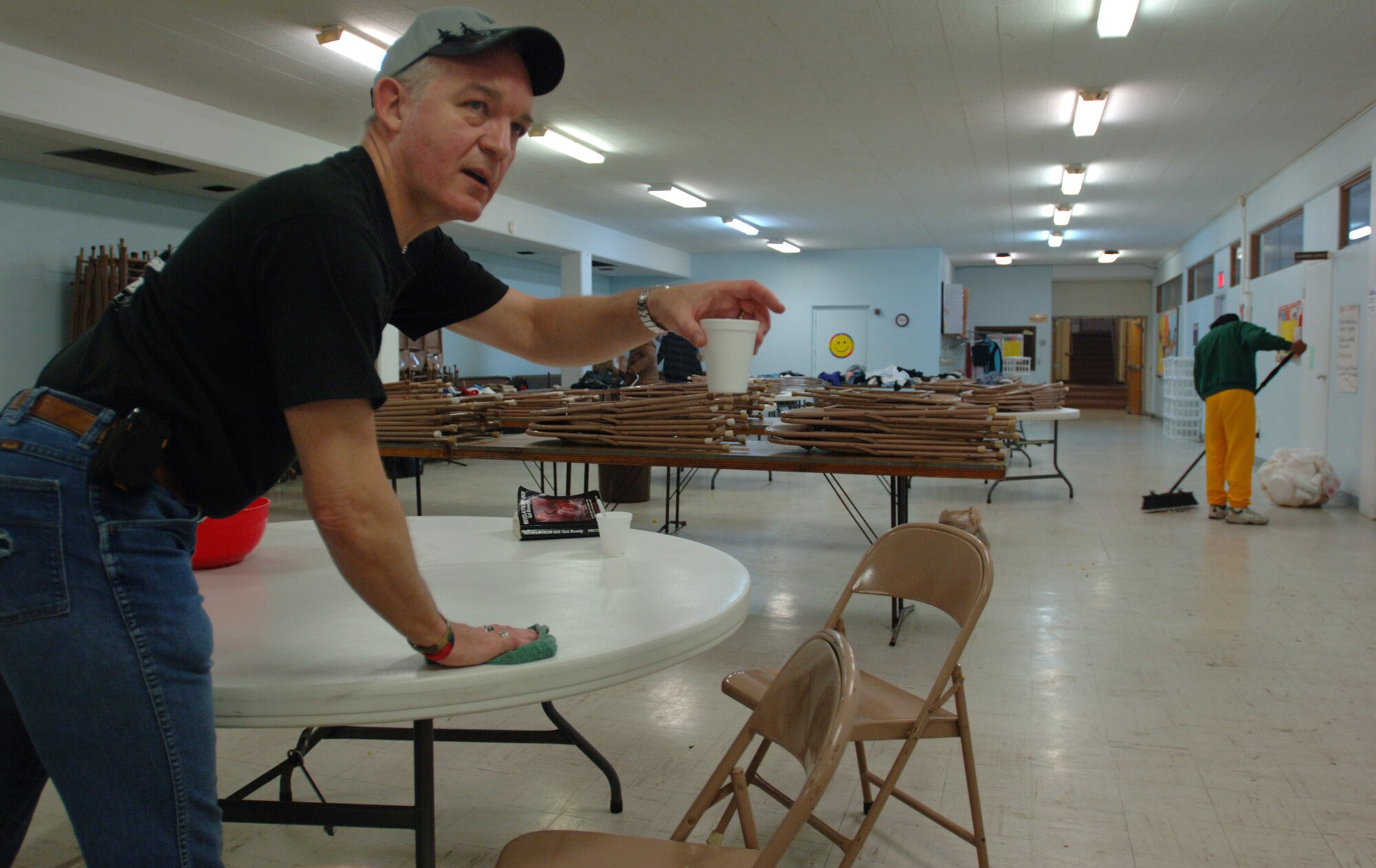 Master Sgt. Bob Livingston looks for help with an abandoned cup while he washes a table used during a free breakfast at a church near downtown Wichita, Kan. Behind him, some done eating look through piles of donated clothes and another helps to sweep the floor.  Homeless men make up the majority of those who travel, usually by foot, for the free meal.  Sergeant Livingston volunteers to support the breakfast every month.  He is the first sergeant of three sections of the 931st Air Refueling Group. (U.S. Air Force photo/Tech. Sgt. Jason Schaap)