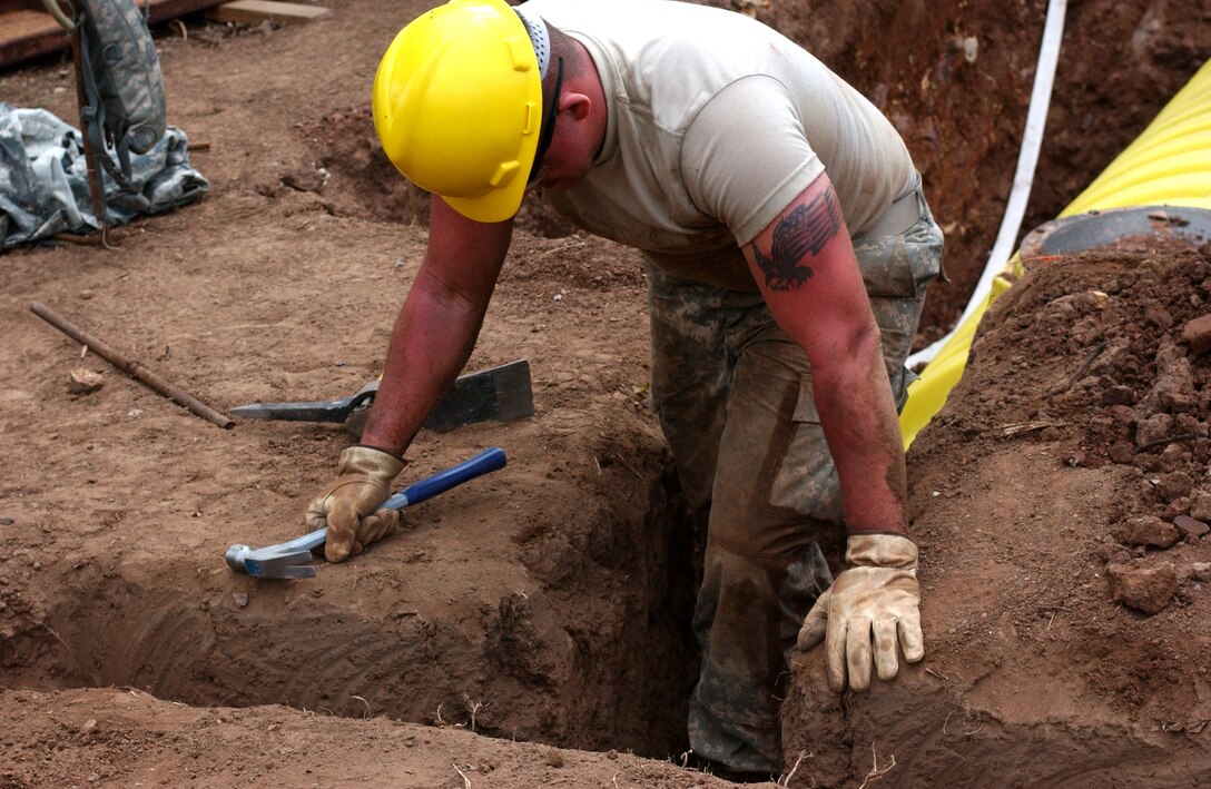 LAS MESAS, HON - Spc. Joshua Winicki, 322nd Engineer Company, Decorah, Iowa, uses his boots to flatten loose dirt in a narrow trench that he has been digging for a new latrine here April 16. Photo by Staff Sgt. Danny McCormick, Beyond the Horizon public affairs.