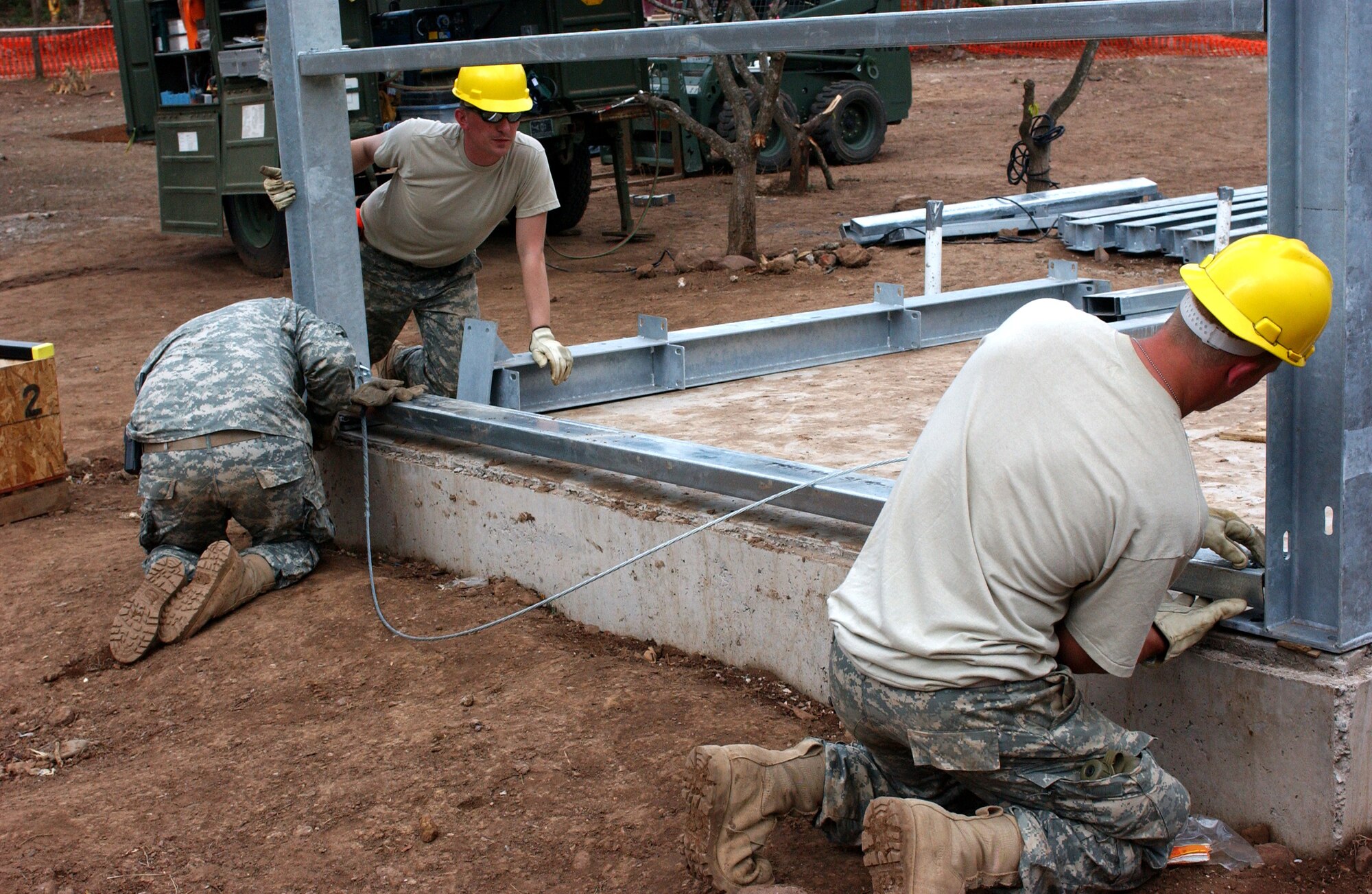 LAS MESAS, HON - Spc. Jesse Brennan (right), Spc. Dustin Roberts (ACU) and Sgt. Gabriel Feuerhelm, all of the 322nd Engineer Company, Decorah, Iowa, attach a bottom brace to the steel framework wall of a new latrine that they are building here April 16. Photo by Staff Sgt. Danny McCormick, Beyond the Horizon public affairs.
