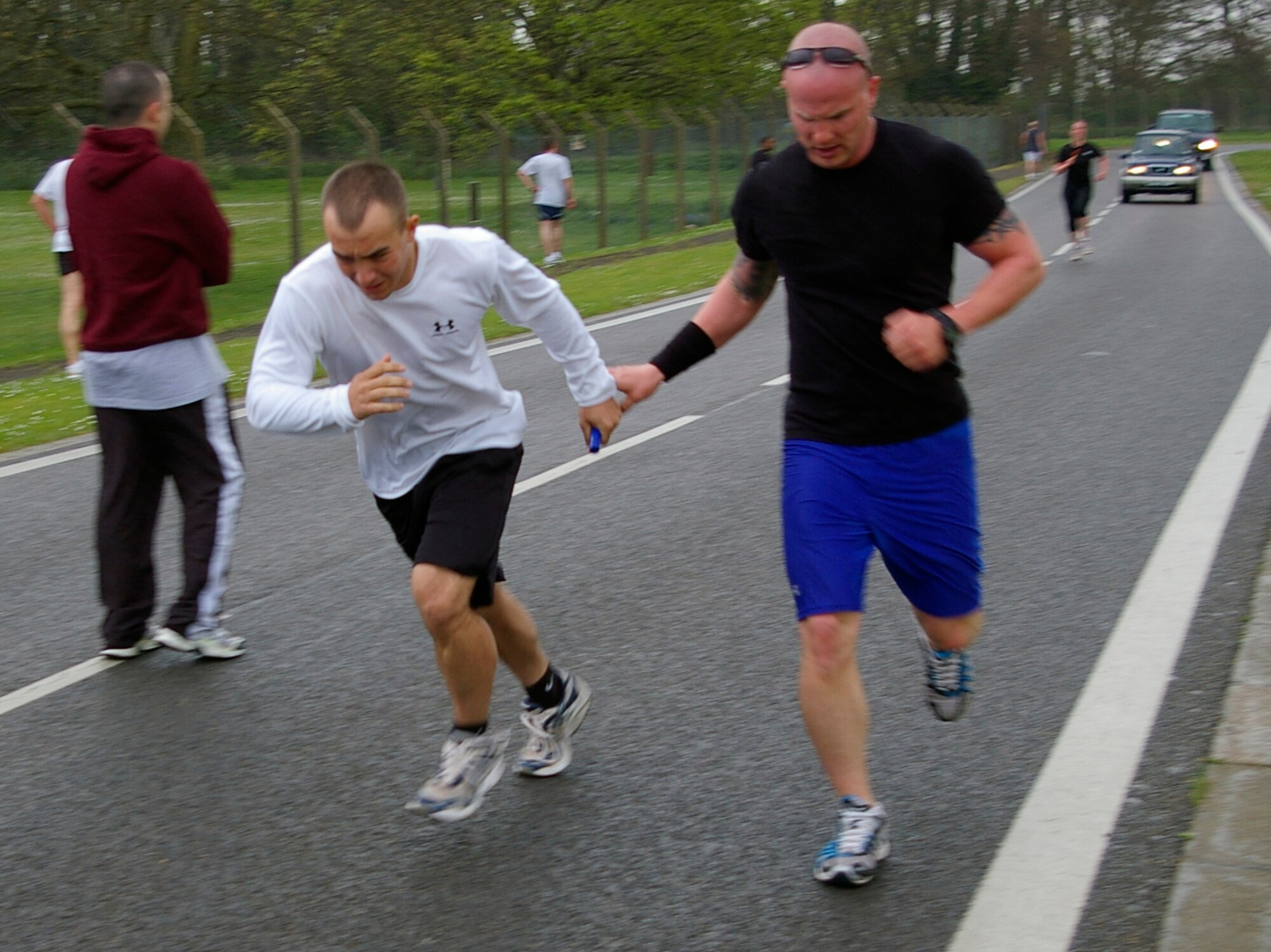 Staff Sgt. Clinton Petit, right, 100th Security Forces Squadron, passes the baton to fellow team-mate, Airman 1st Class Albert Wood, also 100th SFS, during the Air Force Assistance Fund 5 mile run April 29 on the perimeter road running  area on the southside of base. Eleven teams, each with five runners, ran relays in the pouring rain to raise money for the Air Force Assistance Fund. (U.S. Air Force photo by Karen Abeyasekere)