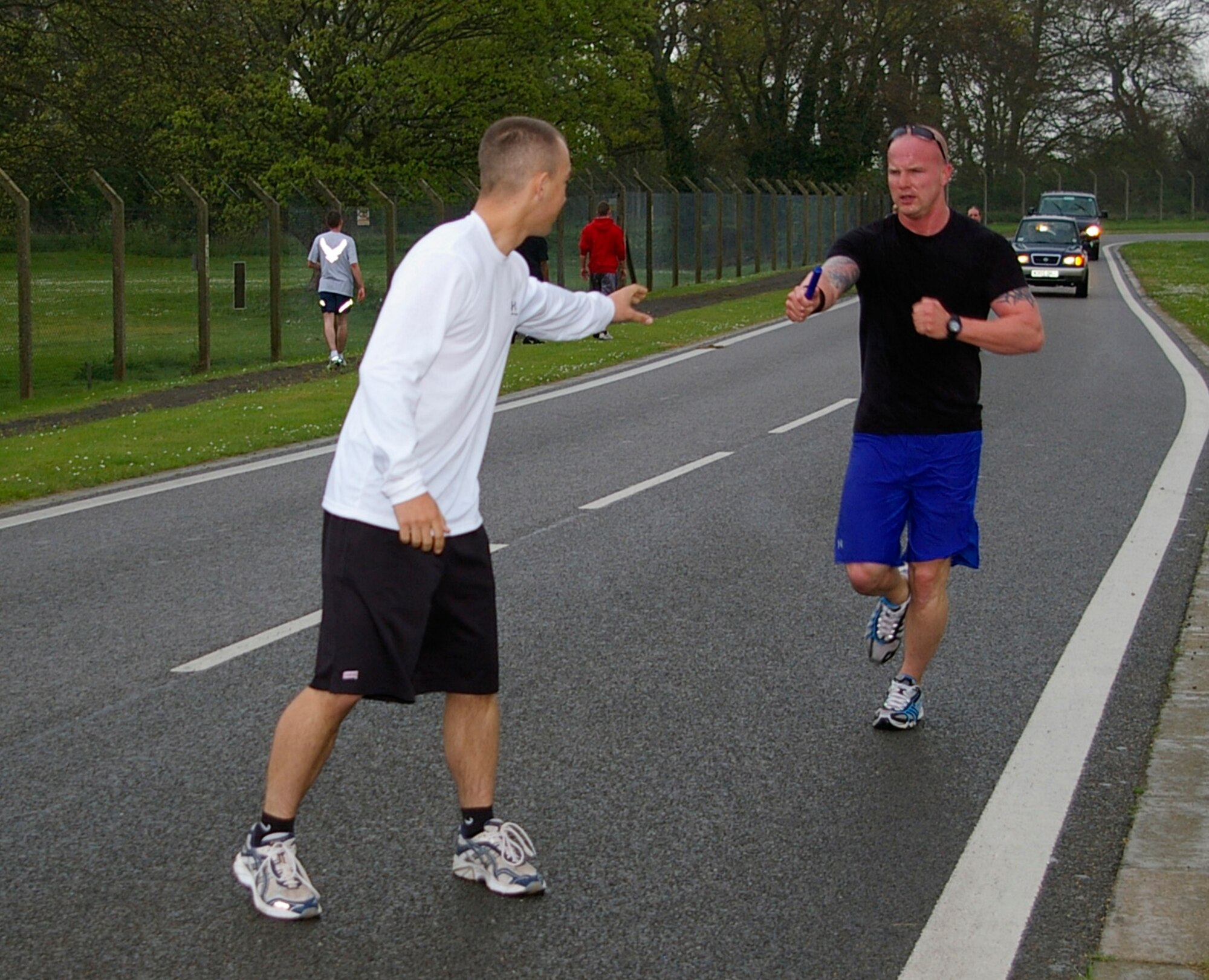 Staff Sgt. Clinton Petit, right, 100th Security Forces Squadron, passes the baton to fellow team-mate, Airman 1st Class Albert Wood, also 100th SFS, during the Air Force Assistance Fund 5 mile run April 29 on the perimeter road running  area on the southside of base. Eleven teams, each with five runners, ran relays in the pouring rain to raise money for the Air Force Assistance Fund. (U.S. Air Force photo by Karen Abeyasekere)