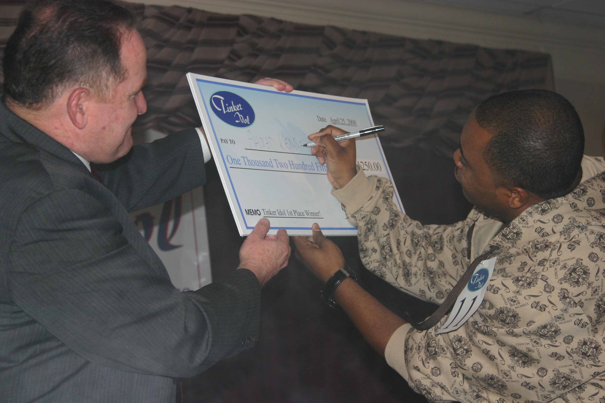 With 72nd Services Director Dan Bell watching, Staff Sgt. Ahmad Kennedy signs his name to a check  as the first ever Tinker Idol.  Sergeant Kennedy will perform the national anthem tonight at the Boxing Smoker at Gerrity Fitness and Sports Center, Bldg. 6004.  Doors open at 6 p.m.  (Air Force photo by Kimberly Woodruff)