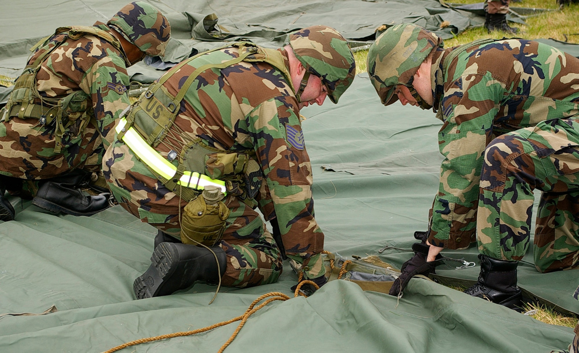 Tech. Sgt. Michael Liston, left, and Staff Sgt. James Blackburn, both 100th CES Fire Department, work together to join an outer cover for one of the tents at the training site on the southside of base. The Airmen slept in tents overnight as part of their field training exercise. (U.S. Air Force photo by Karen Abeyasekere)