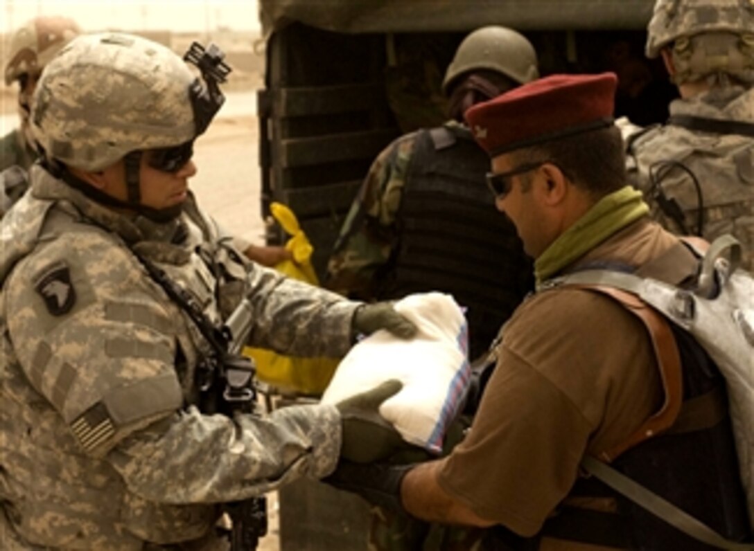 U.S. Army Cpl. David Silva, assigned to the 511th Military Police Company, passes a package of food supplies to an Iraqi police officer for distribution in Zuwerijat, a district of Al Kut, Iraq, April 30, 2008.

