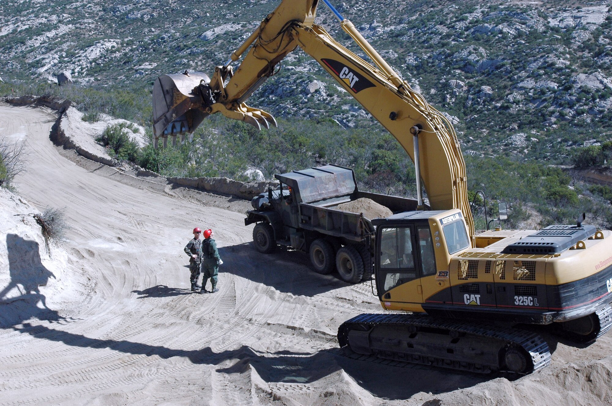 Under the shadow of a large excavator, Staff Sgt. Mark Ellis and Master Sgt. Chris Blackwell discuss plans to smooth out this dangerous stretch of hairpin turns that hamper Border Patrol officers in their efforts to secure the border May 1 near Campo, Calif. Sergeants Ellis and Blackwell are airfield crew specialists from the 201st RED HORSE Squadron from Fort Indiantown Gap, Pa. (U.S. Air Force photo/1st Lt. Jay Ostrich)
