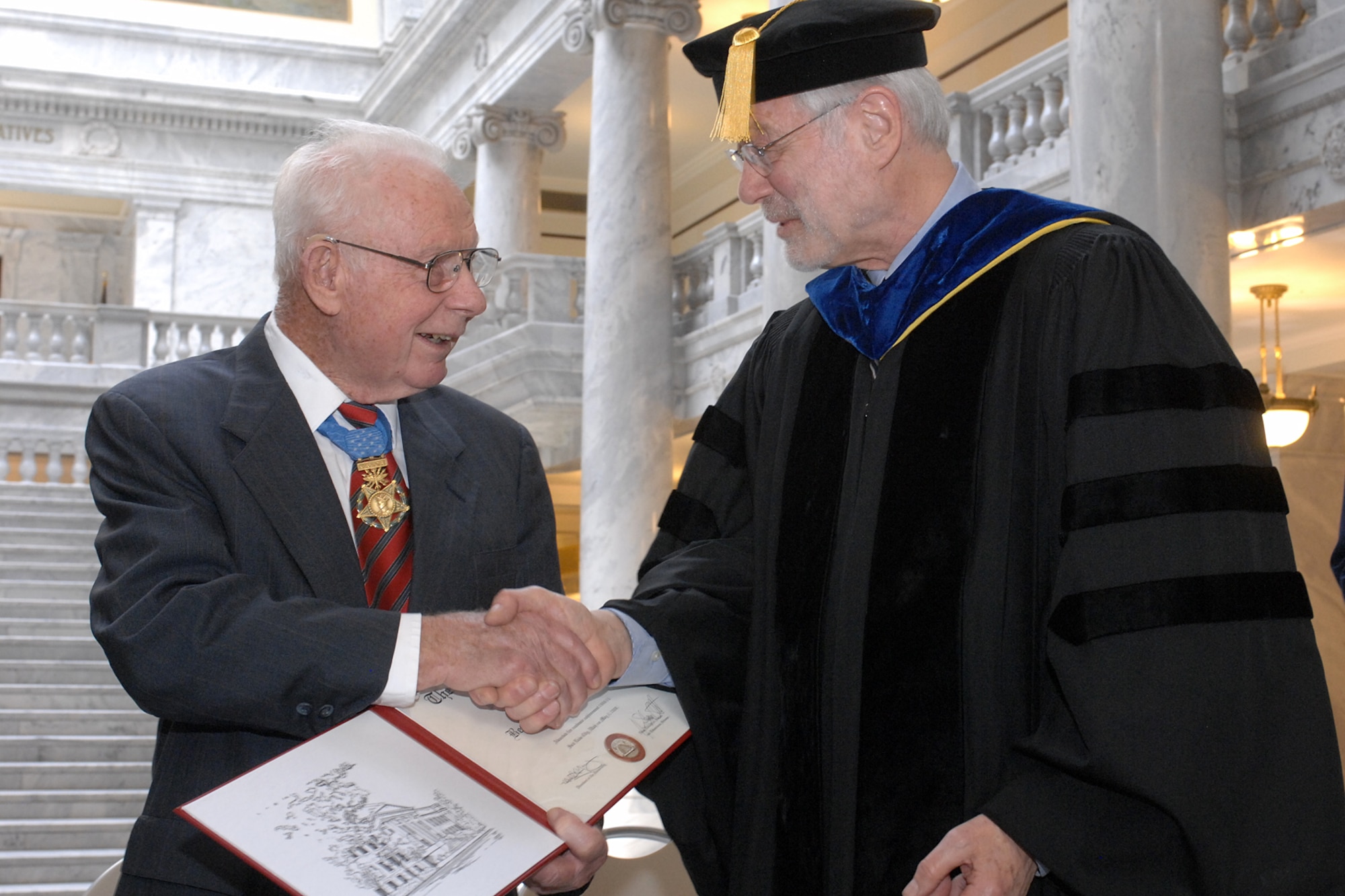 The 81-year-old retired Col. Bernard F. Fisher shakes hands with J. Steven Ott, University of Utah Dean of the College of Social and Behavioral Science, after receiving his Bachelors of Fine Arts May 3. (U.S. Air Force Photo by Alex R. Lloyd)