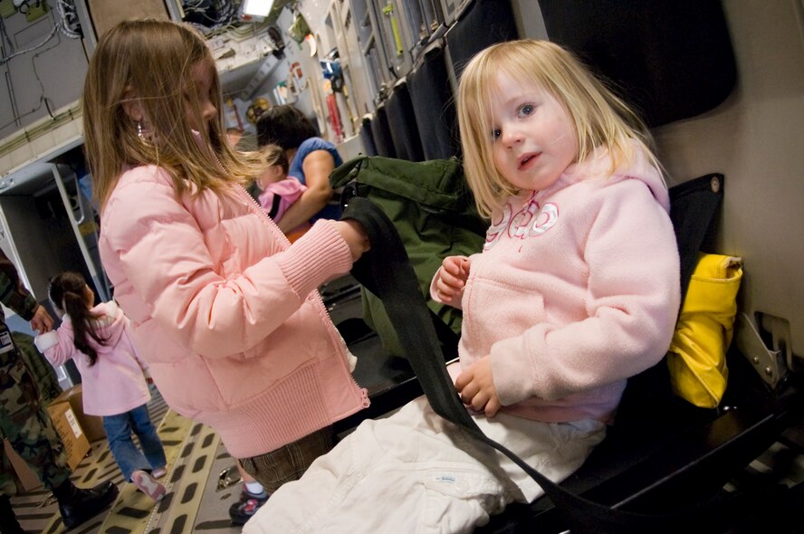 Breanna Warren, 2, waits patiently to be secured to her seat while her older sister Olivia, 5, performs a mockre-flight inspection of the safety belt.