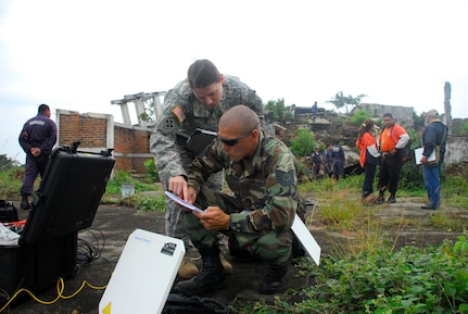 From the grounds of a collapsed and abandoned coffee factory, Joint Task Force-Bravo civil engineers Air Force Tech. Sgt. Mike Vaughn and Army Capt. Sarah Williams set up a field video teleconferencing unit to send imagery gathered here to the United States to assist with the exercise Fuerzas Aliadas Humanitarias 2008, a regional disaster relief exercise involving military and civilian agencies occurring here May 5-15. By capturing imagery of damage from a 2001 earthquake, participants in the exercise have a simulated yet realistic view of damage to help them make accurate decisions regarding the relief process. (U.S. Air Force photo by Tech. Sgt. William Farrow)