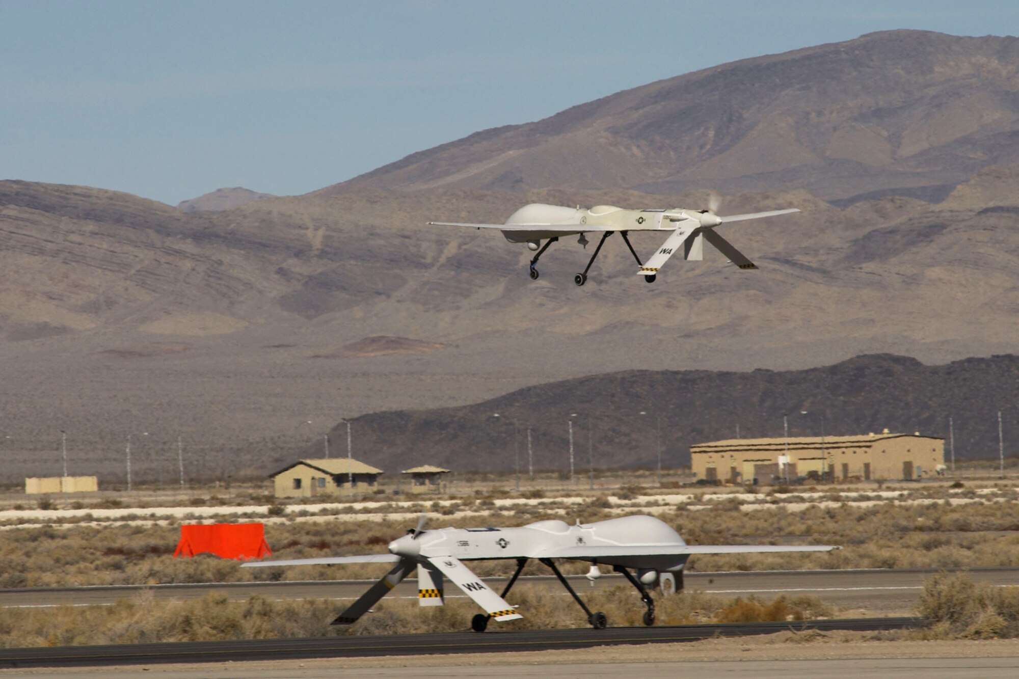 An MQ-1 Predator unmanned aerial vehicle makes a low approach while another waits for takeoff clearance at Creech Air Force Base, Nev. The 11th Reconnaissance Squadron at Creech AFB prepares pilots, sensor operators and other specialists for worldwide intelligence, surveillance and reconnaissance missions worldwide. The Predator can carry two Hellfire air-to-surface missiles in addition to various cameras and synthetic-aperture radar. (U.S. Air Force photo/Master Sgt Robert W. Valenca)