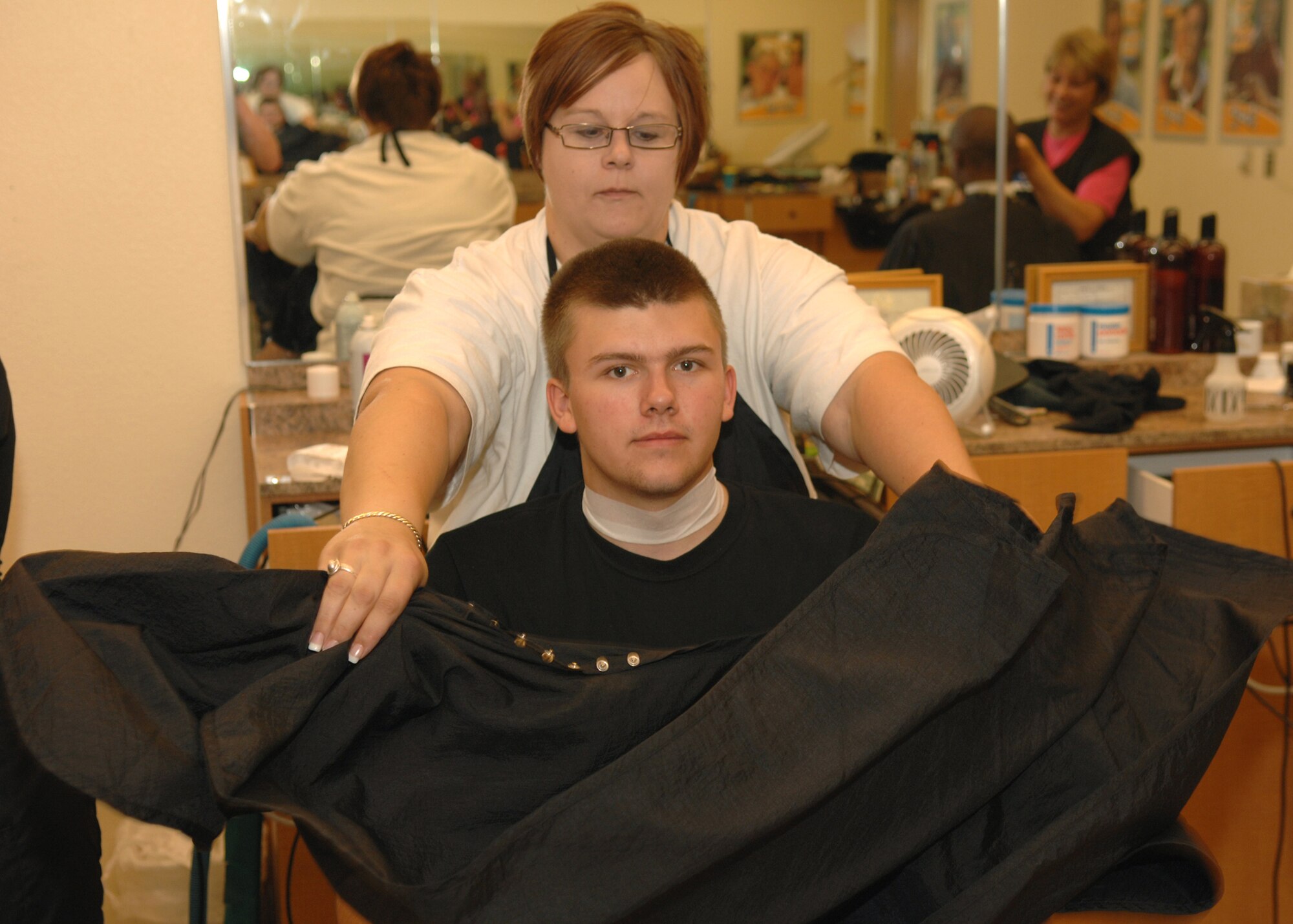 DYESS AIR FORCE BASE, Texas -- AAFES Shayla Billeter places a drape over Airman 1st Class Micheal Breaux in preparation for his new haircut at the Base Exchange barber shop May 7. (U.S. Air Force Photo by Airman 1st Class Stephen Reyes)