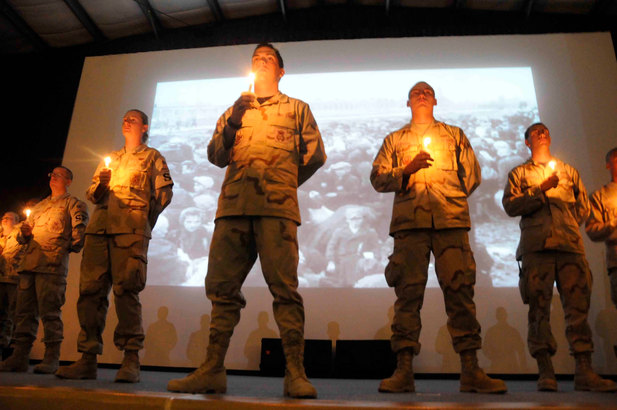 Deployed Airmen hold candles on stage as images of Holocaust victims are projected behind them May 2 at a Southwest Asian air base. More than 30 base members here participated in the Holocaust remembrance vigil to commemorate the more than 6 million lives lost during World War II. (U.S. Air Force photo/Senior Airman Domonique Simmons) 
