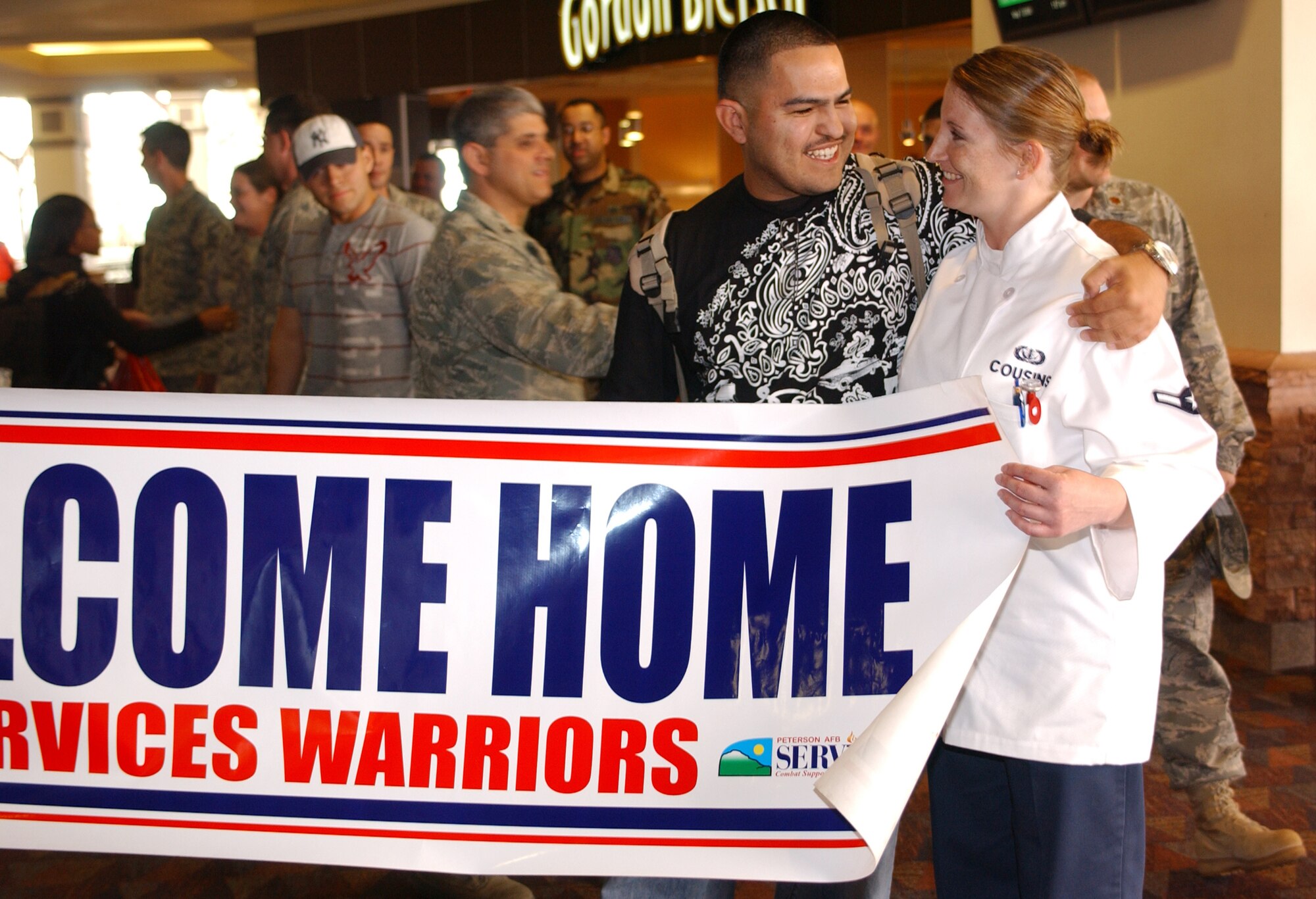 Holding a “welcome home” banner, Airman Mary Cousins welcomes home from deployment fellow squadron member Airman 1st Class Rosbiel Ocanas May 7 at the Colorado Springs airport. Airman Ocanas re-deployed with members of both the 21st Services and Space Communications Squadrons after four-and six-month deployments to Southwest Asia. Both Airmen Cousins and Ocanas are assigned to the 21st SVS. (U.S. Air Force photo/Margie Arnold)