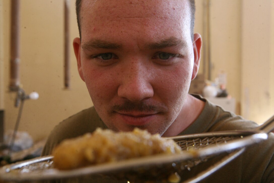 Checking the status of a fried chicken finger, Cpl. Robert J. Hardesty, a food service specialist with Team Mustang, 2nd Light Armored Reconnaissance Battalion, Regimental Combat Team 5, cooks a variety of foods for other Marines with Team Mustang at Combat Outpost Patton, Iraq, May 8. While Team Mustang continues their mission securing the main highways of Iraq , Hardesty, 21, from Goshen, Ind., and Lance Cpl. Thomas L. Jones, a scout with Team Mustang from Chesapeake, Va., will be there to serve hot rations to them.