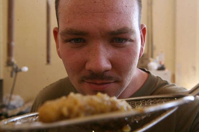 Checking the status of a fried chicken finger, Cpl. Robert J. Hardesty, a food service specialist with Team Mustang, 2nd Light Armored Reconnaissance Battalion, Regimental Combat Team 5, cooks a variety of foods for other Marines with Team Mustang at Combat Outpost Patton, Iraq, May 8. While Team Mustang continues their mission securing the main highways of Iraq , Hardesty, 21, from Goshen, Ind., and Lance Cpl. Thomas L. Jones, a scout with Team Mustang from Chesapeake, Va., will be there to serve hot rations to them.