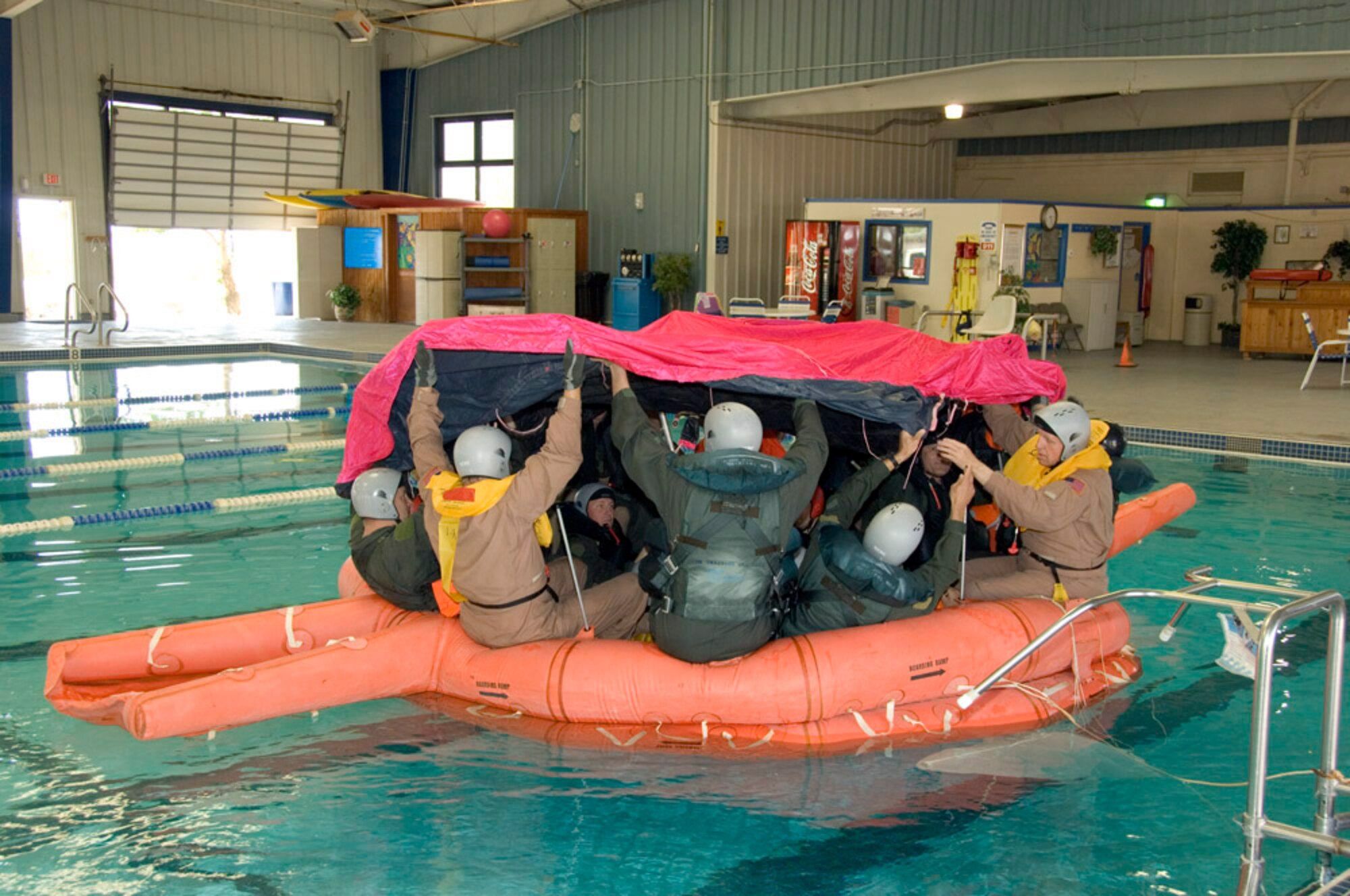 Edwards and NASA Dryden Flight Research Center personnel practice pulling a protective tarp over a 20-person life raft during a joint water survival training session at the Oasis Aquatic Center pool here May 6. The Air Force and NASA students received training on parachuting into water, parachute water drags, parachute canopy entanglement problems, life raft boarding procedures, use of water survival equipment and rescue techniques. (NASA photo by Tony Landis)