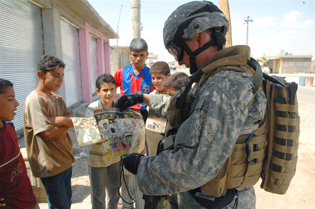 Iraqi children show pictures of the Iraqi soccer team to U.S. Air Force Special Agent "Michael" from the Air Force Office of Special Investigations, during a mission to their village near Kirkuk, Iraq. (U.S. Air Force photo/Staff Sgt. Dallas Edwards)