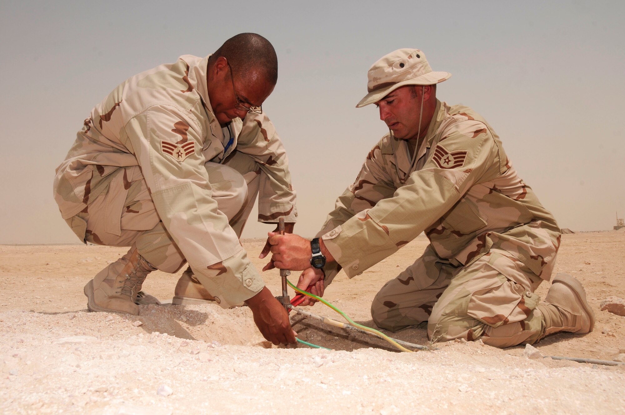 SOTHWEST ASIA--379th Expeditionary Civil Engineer Squadron electric system engineer Senior Airman Mario Hunter (left) steadies a cable while Staff Sgt. Bryan Butcsh tightens it to the grounding rod. More than 30 rods, valued at $100 each, were installed to prevent electronics from grounding or shorting out, safeguarding $193 million of Army assets. (U.S. Air Force Photo/ Senior Airman Domonique Simmons.)
