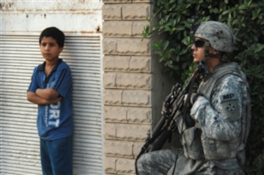 An Iraqi boy stands near U.S. Army Cpl. Christopher Paukei from 3rd Brigade Combat Team, 4th Infantry Division outside a park area in Sadr City, Baghdad, Iraq, on May 3, 2008.  Coalition and Iraqi forces patrol the area in an effort to determine if new barriers around the city are making the residents feel safe.  