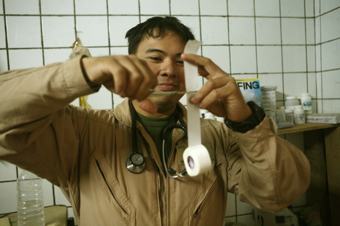 Petty Officer 2nd Class Jason C. Deguzman, a corpsman with Team Mustang, 2nd Light Armored Reconnaissance Battalion, Regimental Combat Team 5, cuts a strip of medical tape at Patrol Base Rio Grande, Iraq, May 10. The sailor, whom Marines with 2nd LAR have nicknamed "Gus," has been awarded two Bronze Star Awards, one with a combat distinguishing device, a Purple Heart and was meritoriously promoted to his present rank for actions in two previous combat tours. "I have always wanted to be a nurse or a doctor," said Deguzman, 24, from Santa Rosa, Calif. "I knew that becoming a Navy corpsman would be the first step for me."