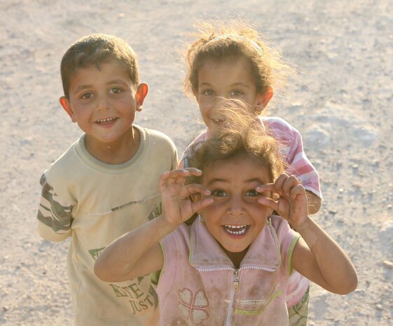 Three children near Baghdadi, Iraq, are all smiles as they await Marines from Combat Outpost Timberwolf to pass out school supplies Saturday. Marines with Headquarters Company, Regimental Combat Team 5, are conducting operations at Combat Outpost Timber Wolf as a provisional rifle platoon. The PRP is made up of non-infantry Marines trained to do a basic rifleman's job. More than 300 pounds of school supplies were donated by the Freemont County School District Number One in Wyoming, which made a school-wide initiative to send school supplies to Iraqi children.